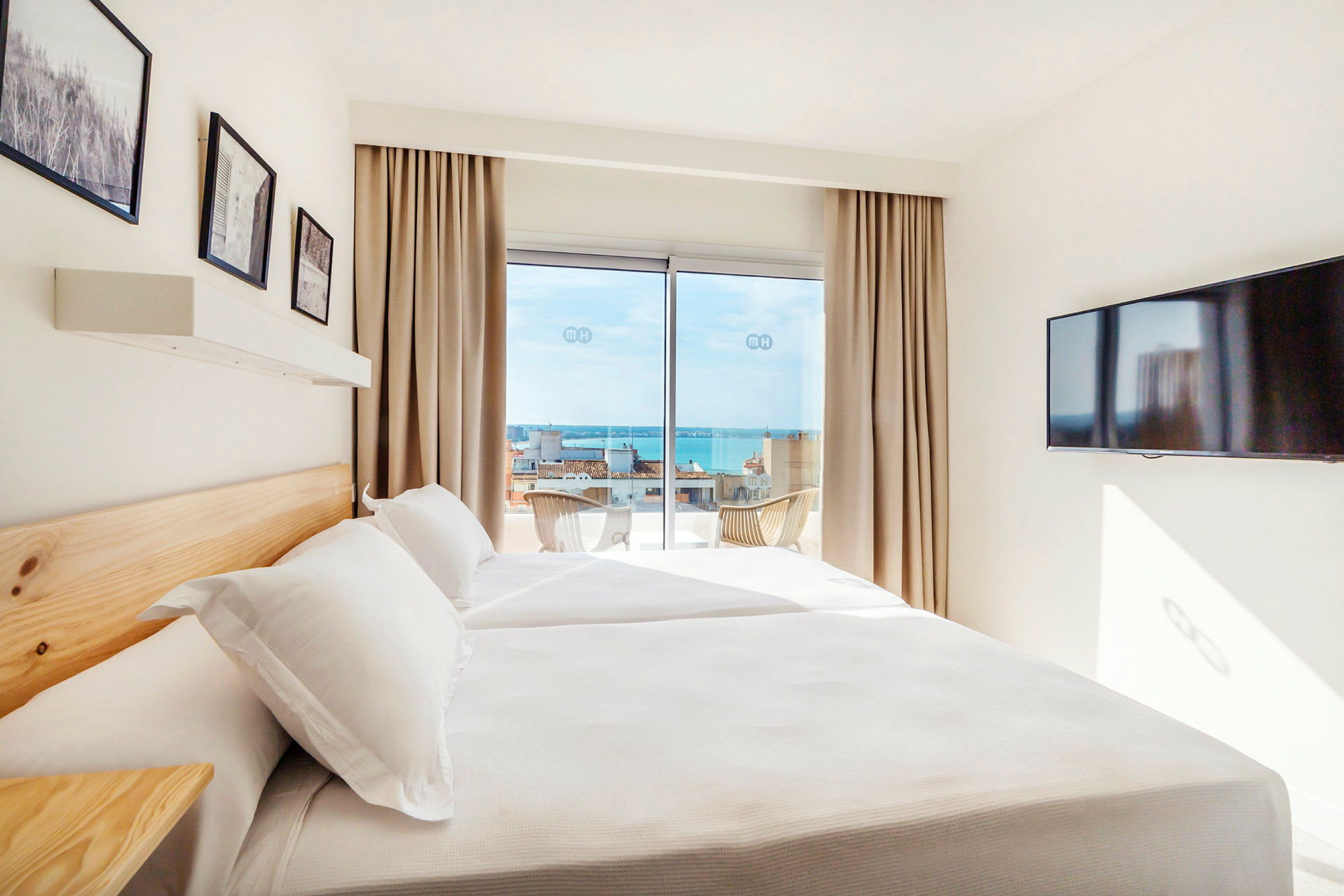 Ett hotellrum med dubbelsäng och stora fönster som visar utsikt över havet. (AI-genererad text)