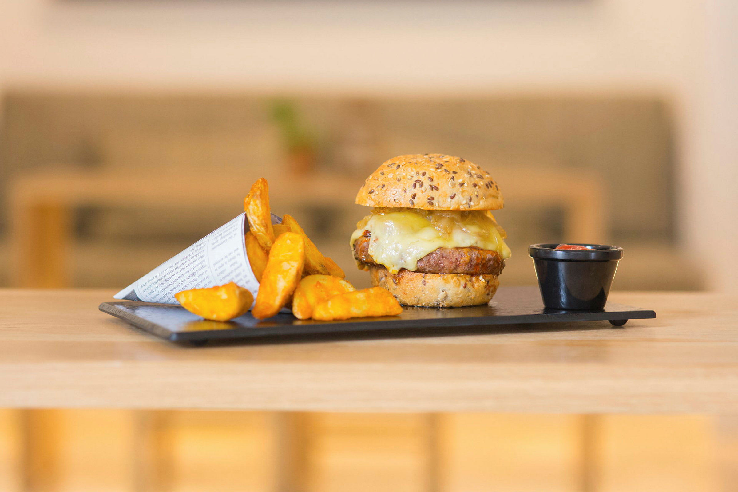 Hamburgare med ost, potatisklyftor och dippsås på en tallrik. (AI-genererad text)