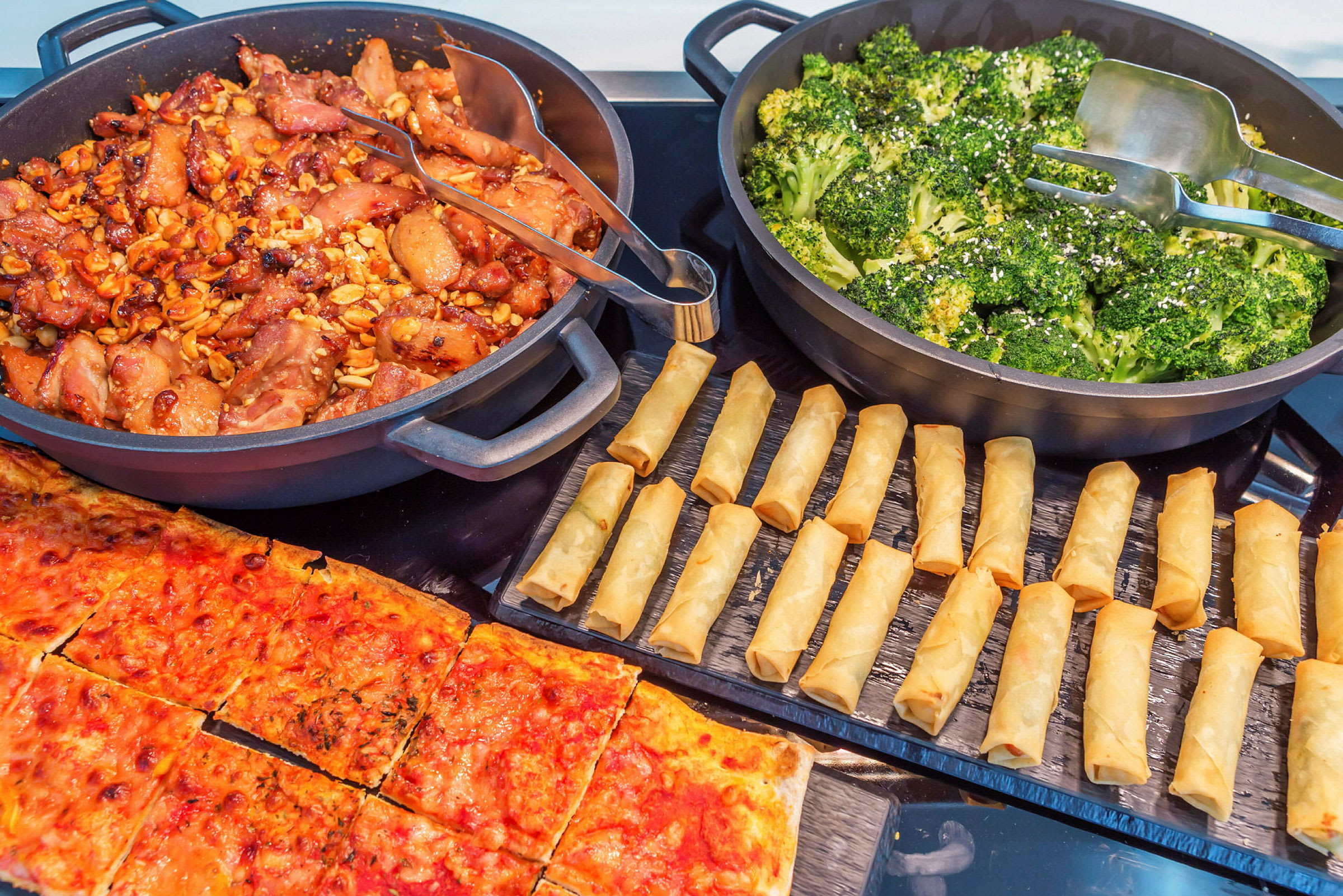 En buffé med olika maträtter, inklusive kyckling, broccoli, vårrullar och pizza. (AI-genererad text)