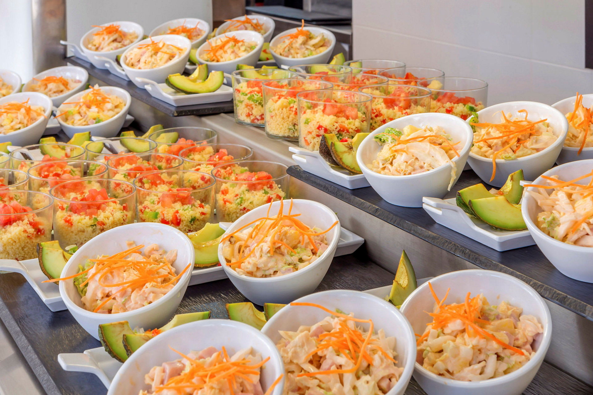 Buffé med små skålar innehållande sallad och avokado samt glas med färgstarka couscousrätter. (AI-genererad text)