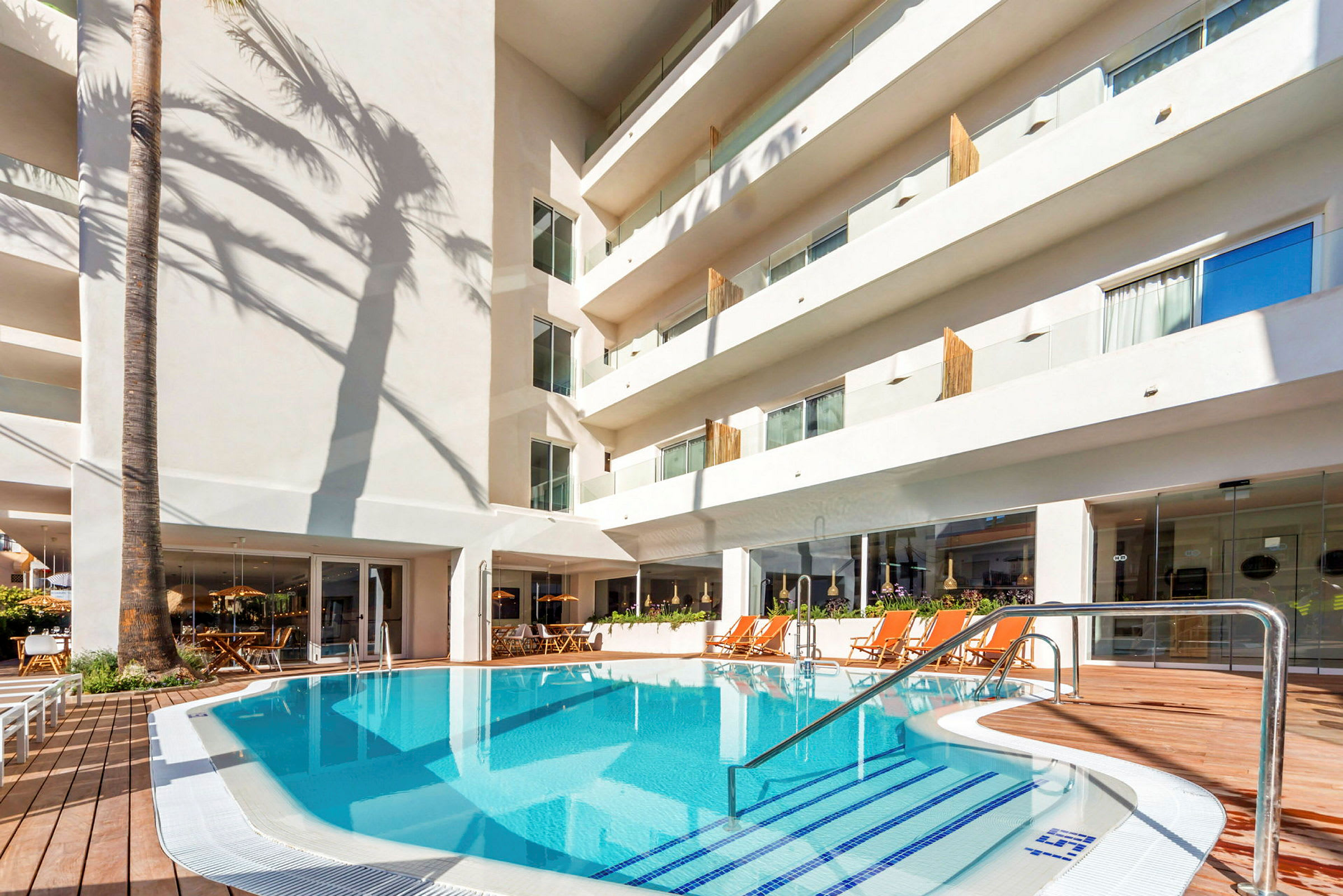 En hotellpool omgiven av solstolar och en vit byggnad. (AI-genererad text)