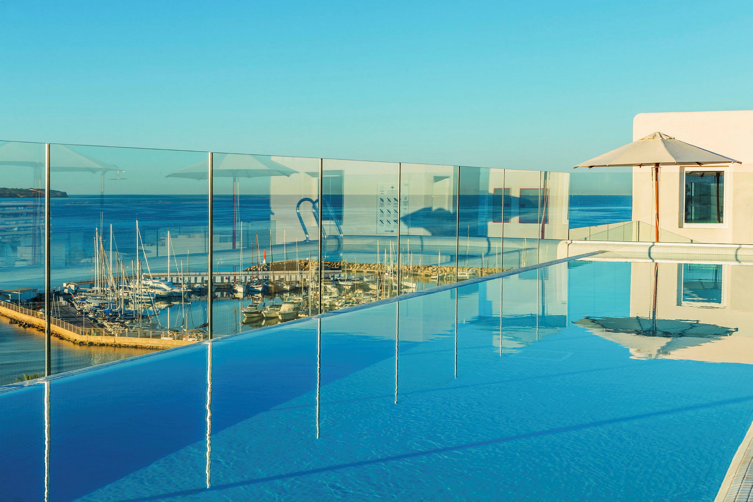 En pool med glasräcke och utsikt mot en hamn med båtar vid havet. (AI-genererad text)