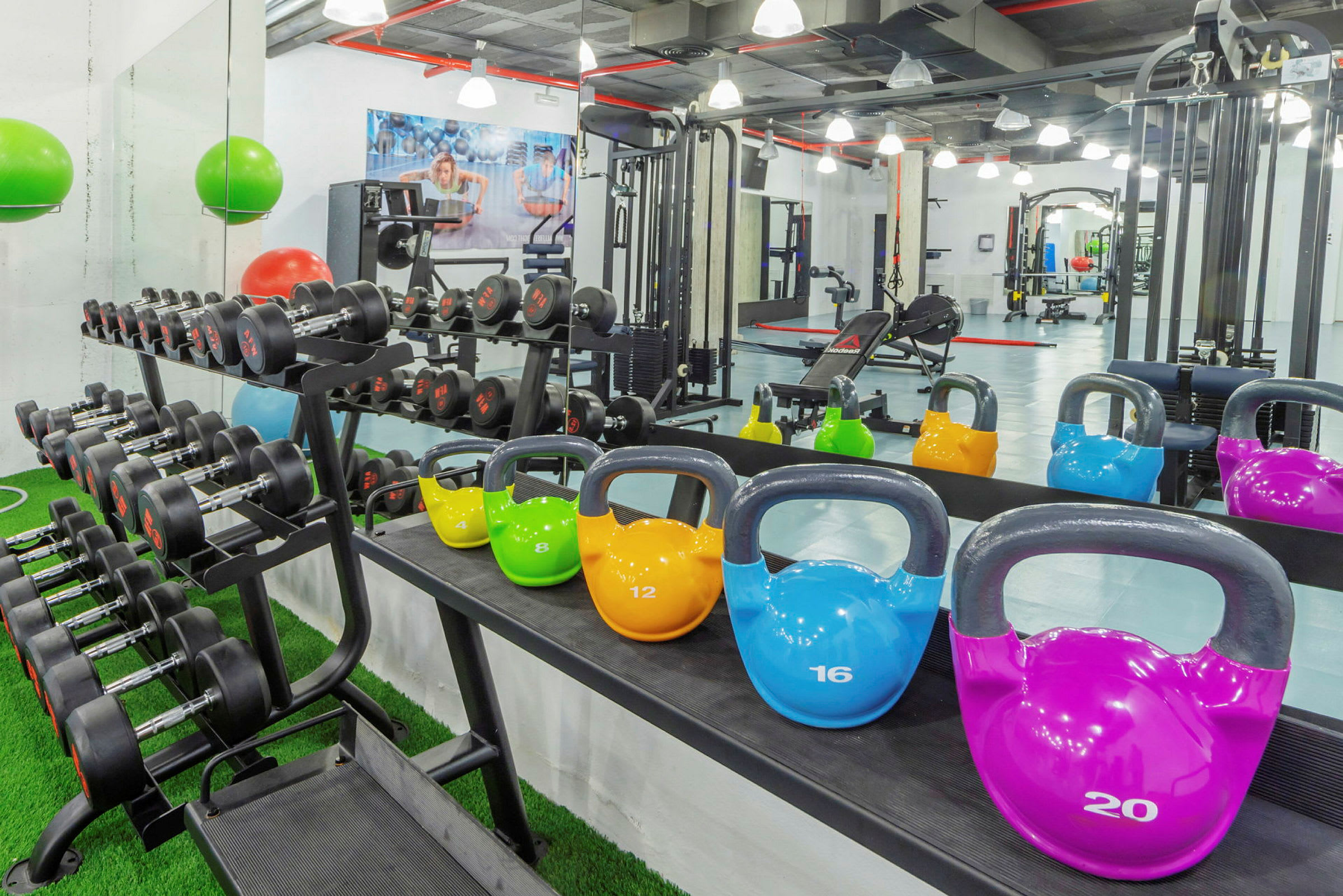 Bild av ett gym med hantlar på ett ställ och kettlebells i olika färger placerade på en hylla, med träningsutrustning i bakgrunden. (AI-genererad text)