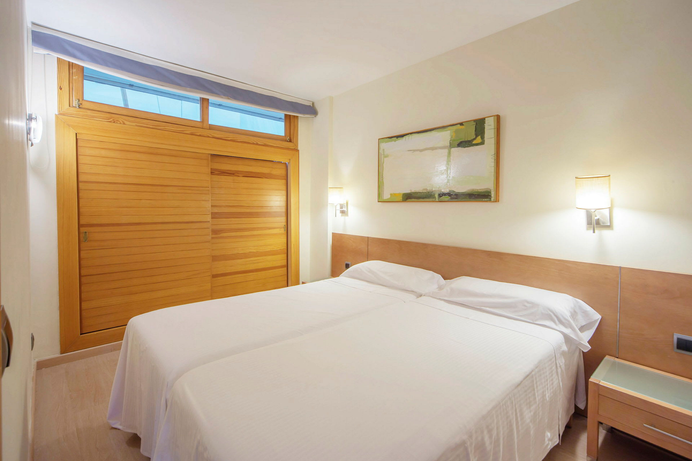 Ett hotellrum med två enkelsängar sammanställda, en trävägg och en tavla på väggen. (AI-genererad text)