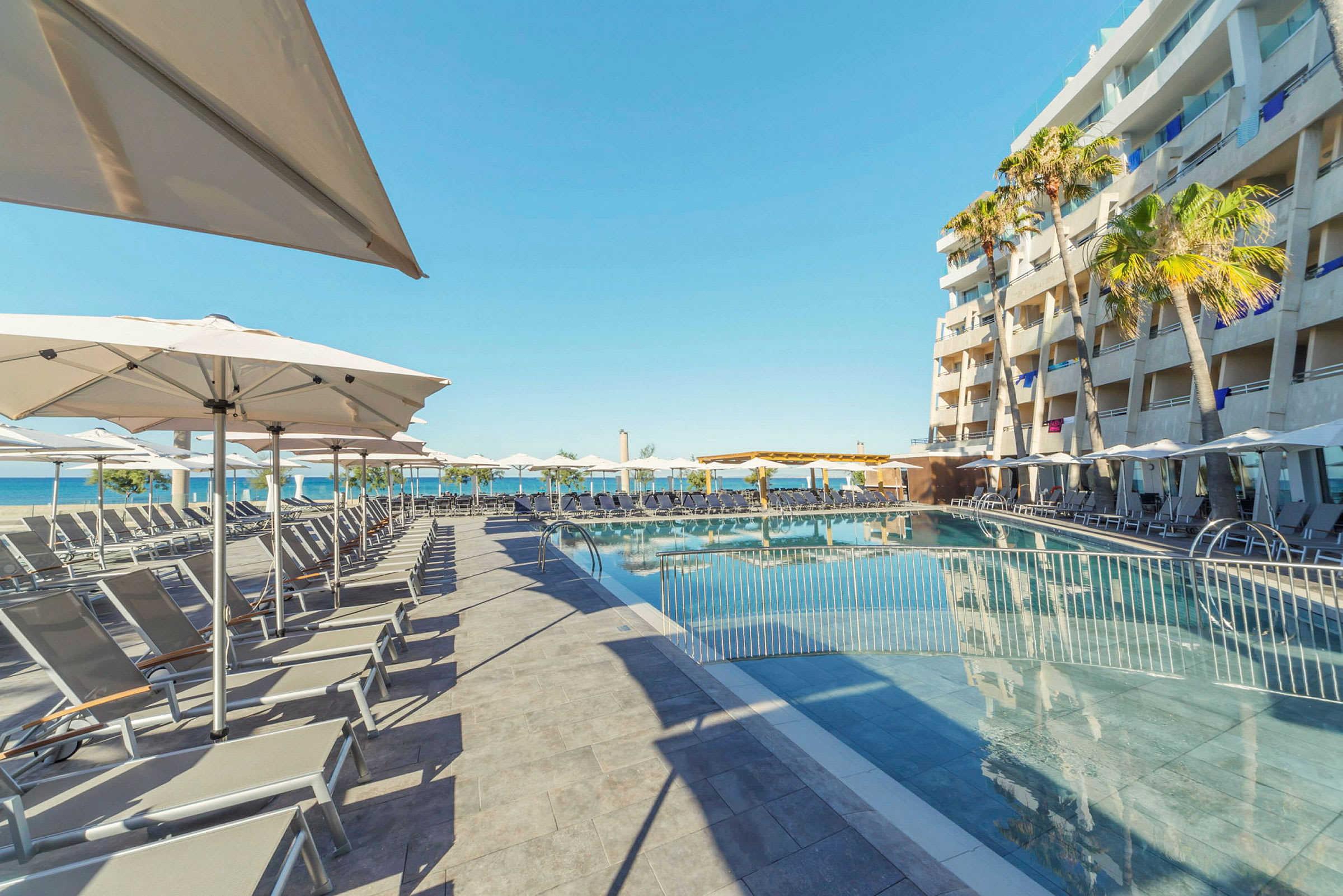En poolområde vid ett hotell, med solstolar, parasoll och en havsutsikt i bakgrunden. (AI-genererad text)