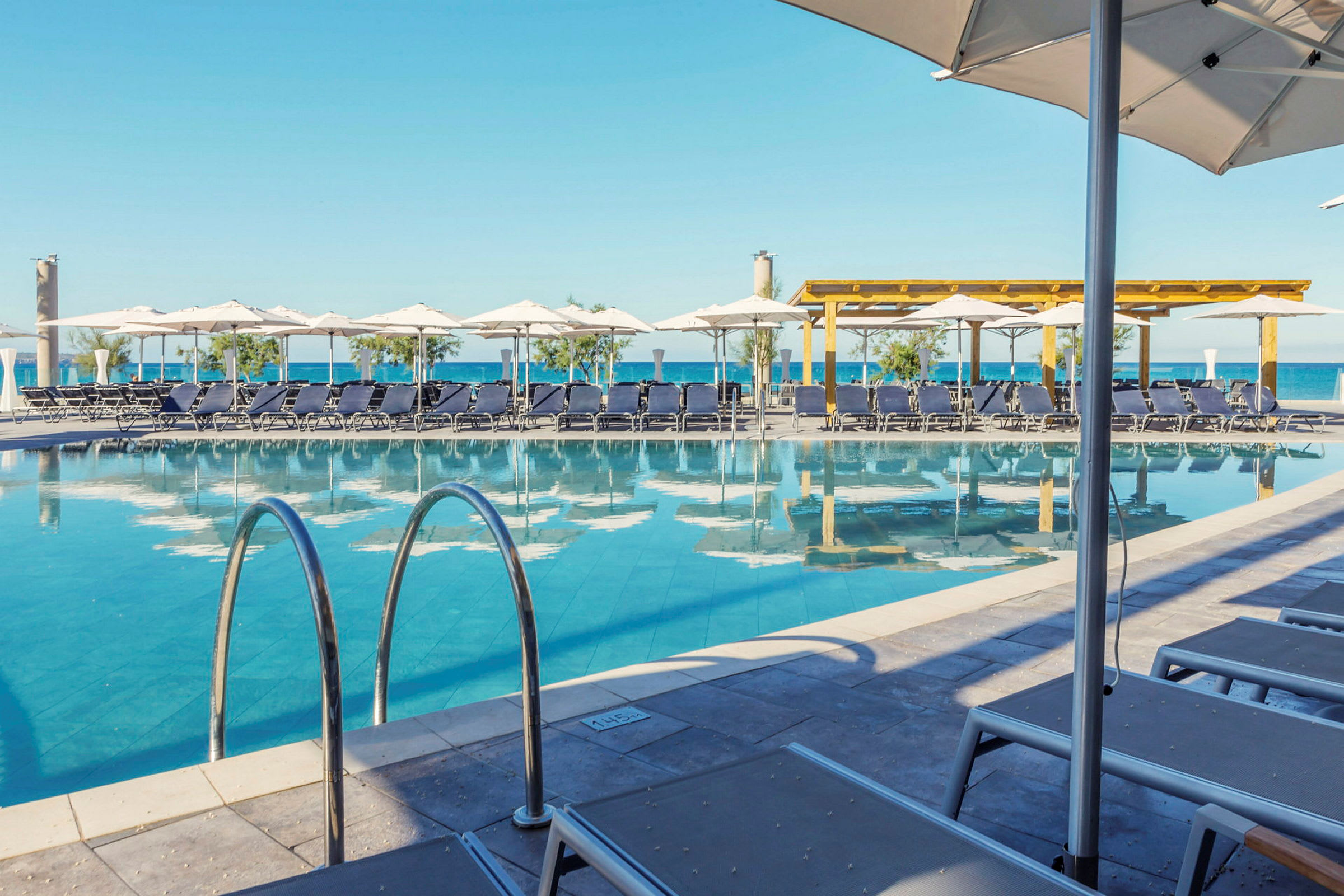 En pool med solstolar och parasoller i en utomhusmiljö nära havet. (AI-genererad text)