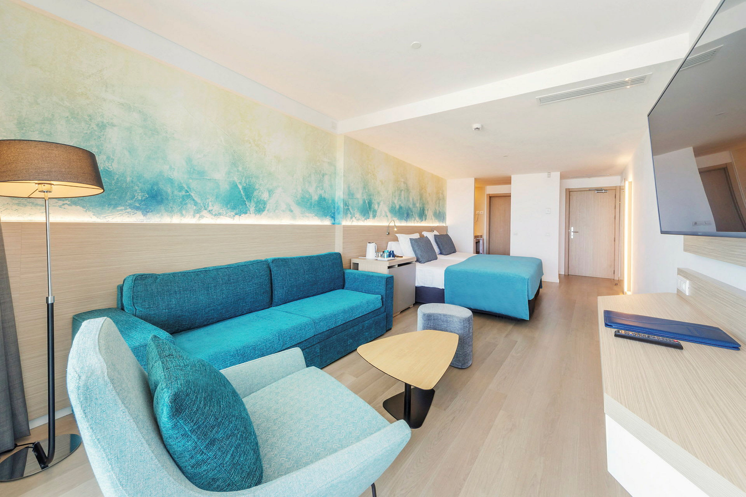 Hotellrum med modern inredning, blå detaljer, och en dubbelsäng. (AI-genererad text)