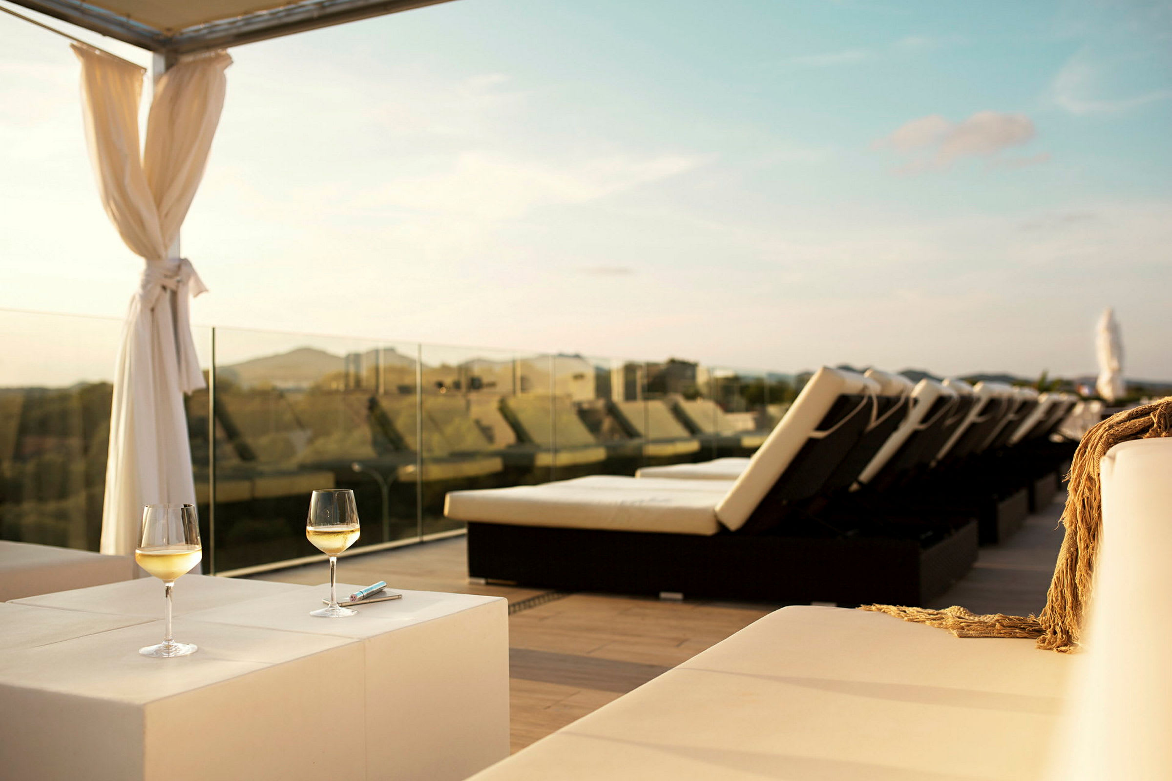 Solterrass med solstolar, två glas vitt vin på ett bord och utsikt över landskapet. (AI-genererad text)