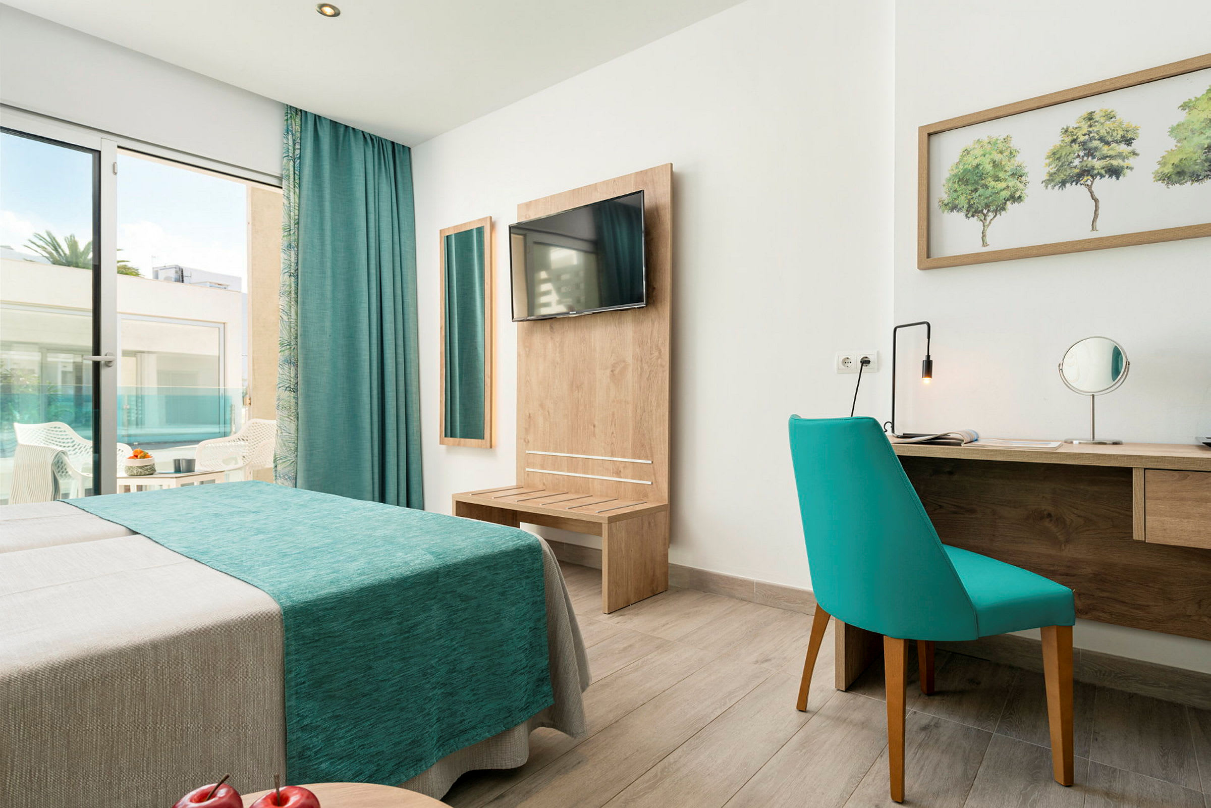 Ett hotellrum med en blå soffa, spegel, skrivbord och en utgång till en balkong. (AI-genererad text)