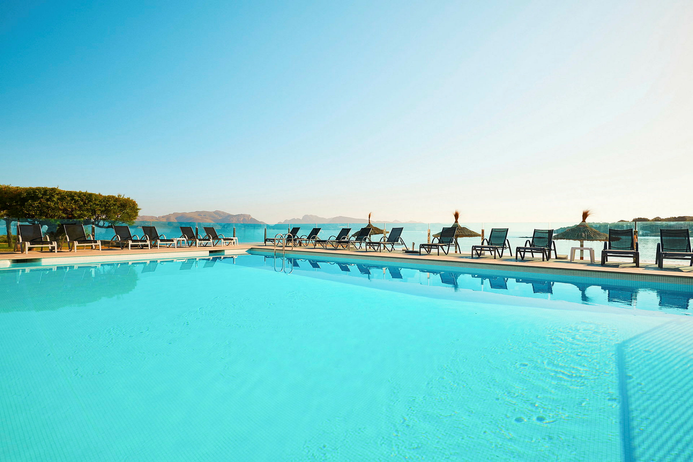 Hotellpool med solstolar och parasoller med havsutsikt. (AI-genererad text)