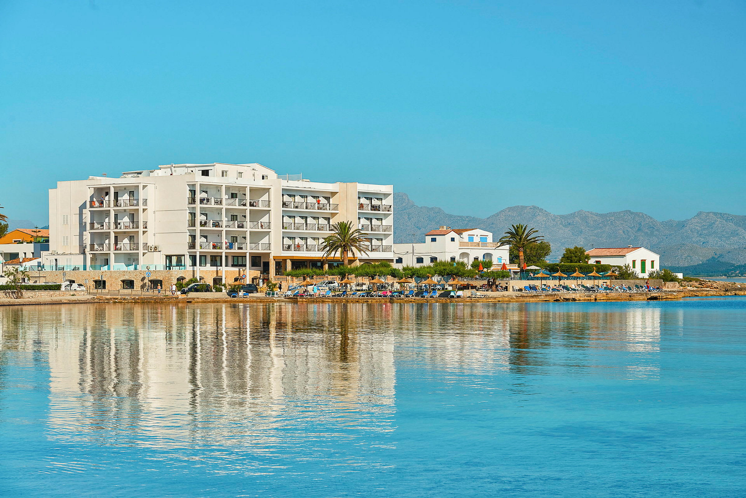 Bild av ett hotell vid stranden med hav och berg i bakgrunden. (AI-genererad text)