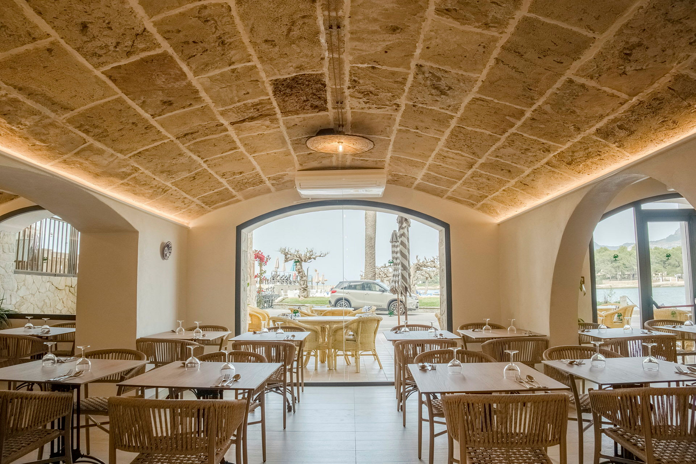 Interiör av en restaurang med stenväggar och valvtak, bord och stolar i trä samt stora fönster som vetter mot utsiktsplatser utomhus. (AI-genererad text)