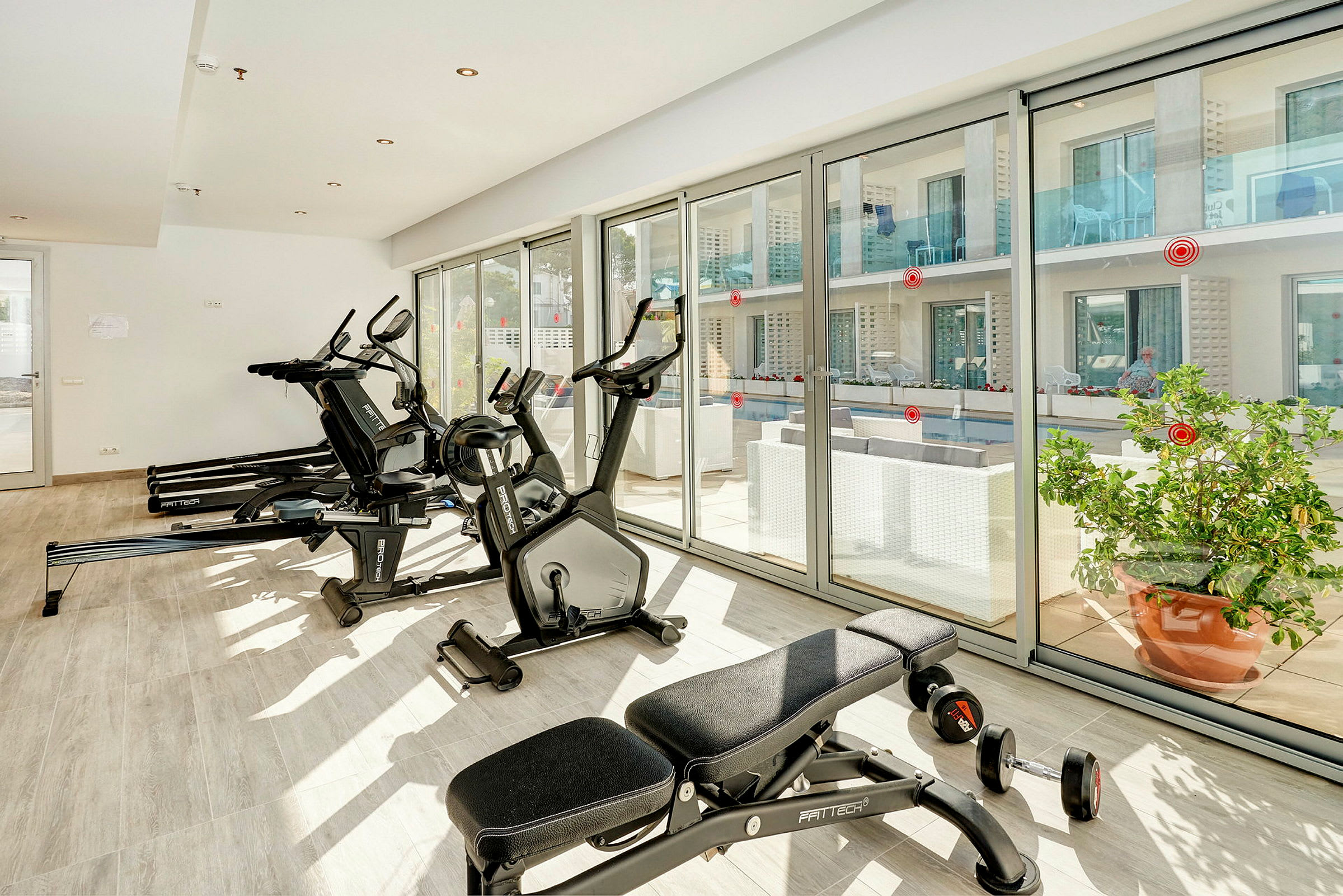Gym med träningsutrustning och stora fönster som vetter mot en uteplats. (AI-genererad text)