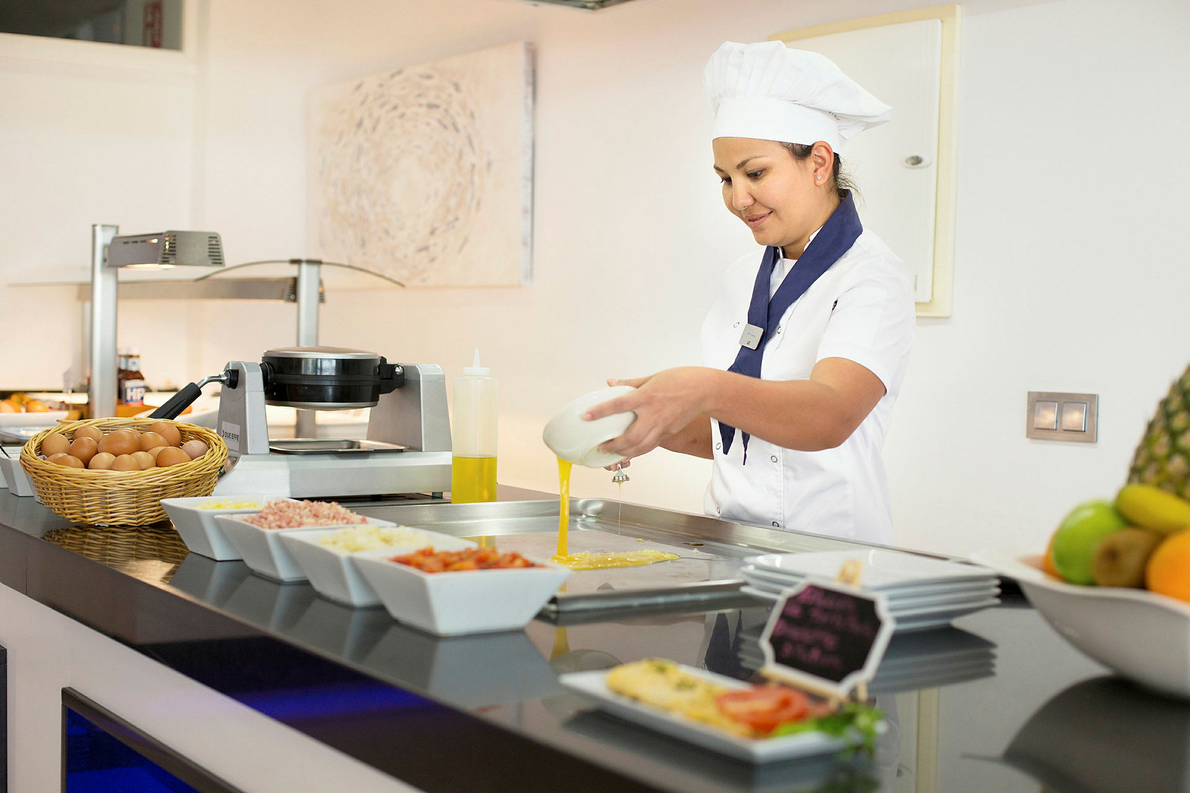 En kock förbereder mat vid en serveringsdisk, omgiven av olika ingredienser i skålar och en korg med ägg. (AI-genererad text)