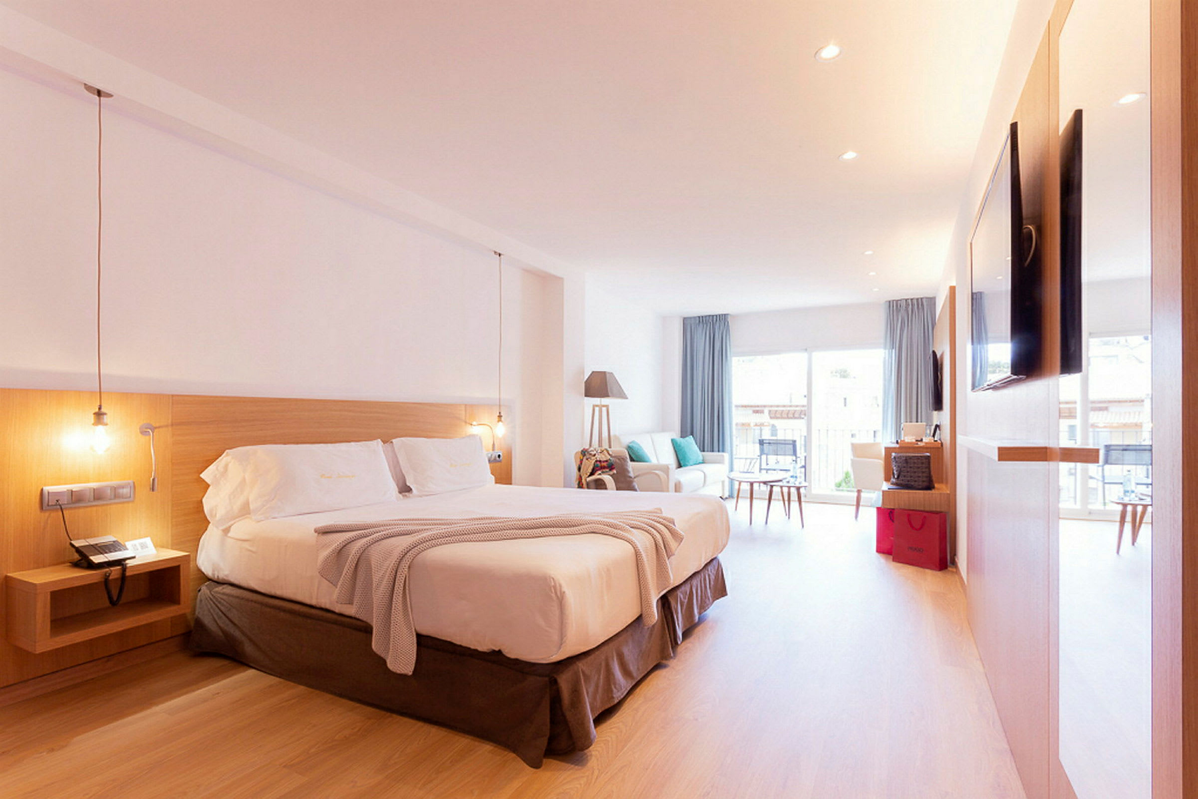 Ett hotellrum med en stor dubbelsäng, ljusa möbler och stora fönster. (AI-genererad text)