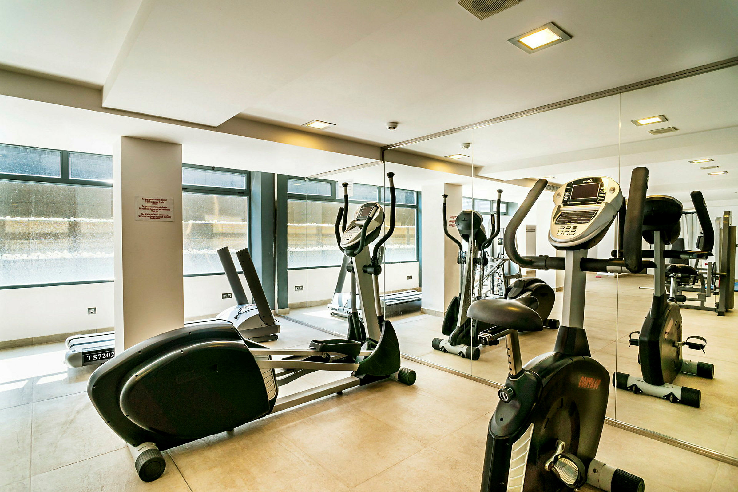 Gym med motionscyklar och träningsutrustning framför en spegel. (AI-genererad text)