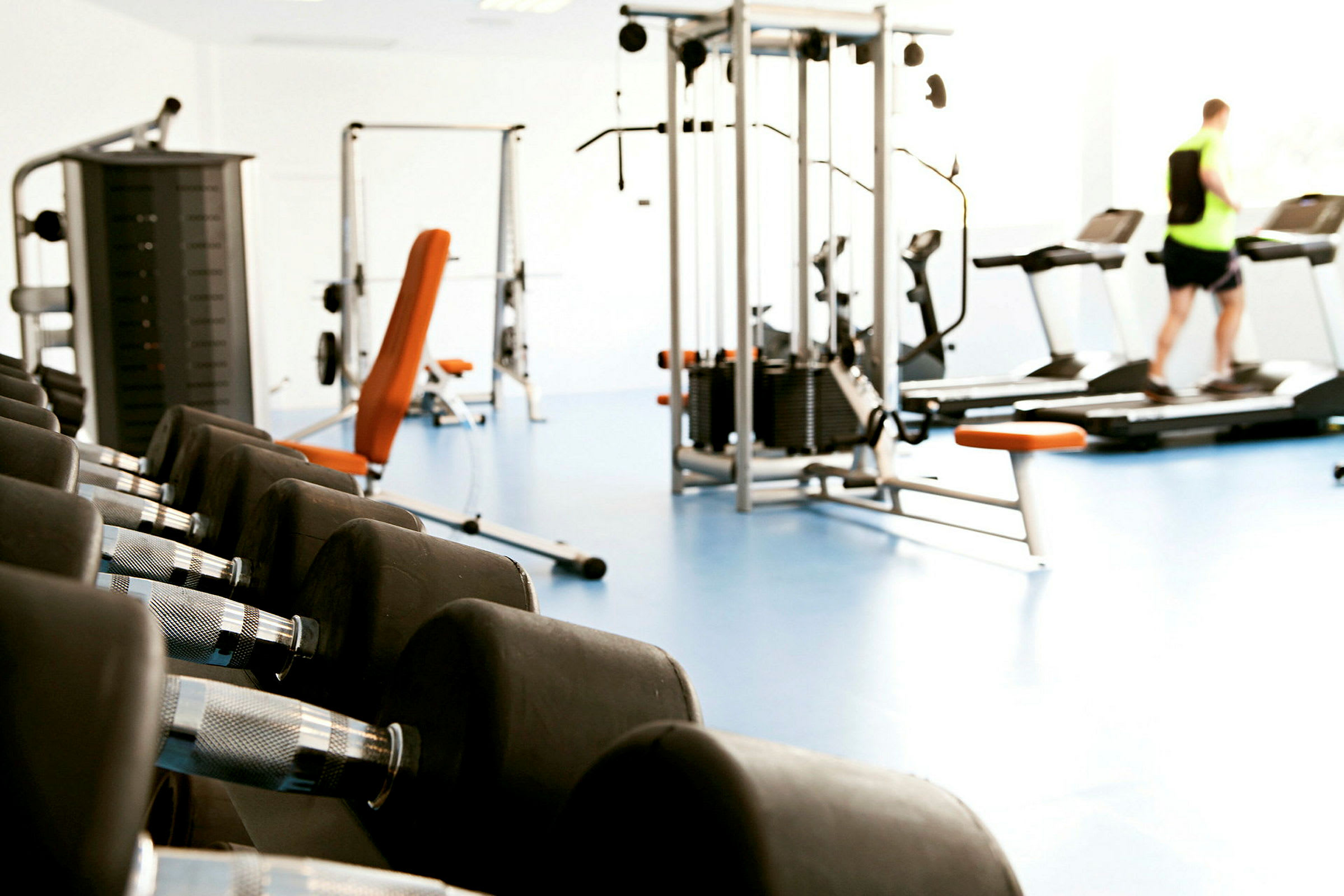 Ett gym med träningsmaskiner, hantlar och en person på löpband. (AI-genererad text)