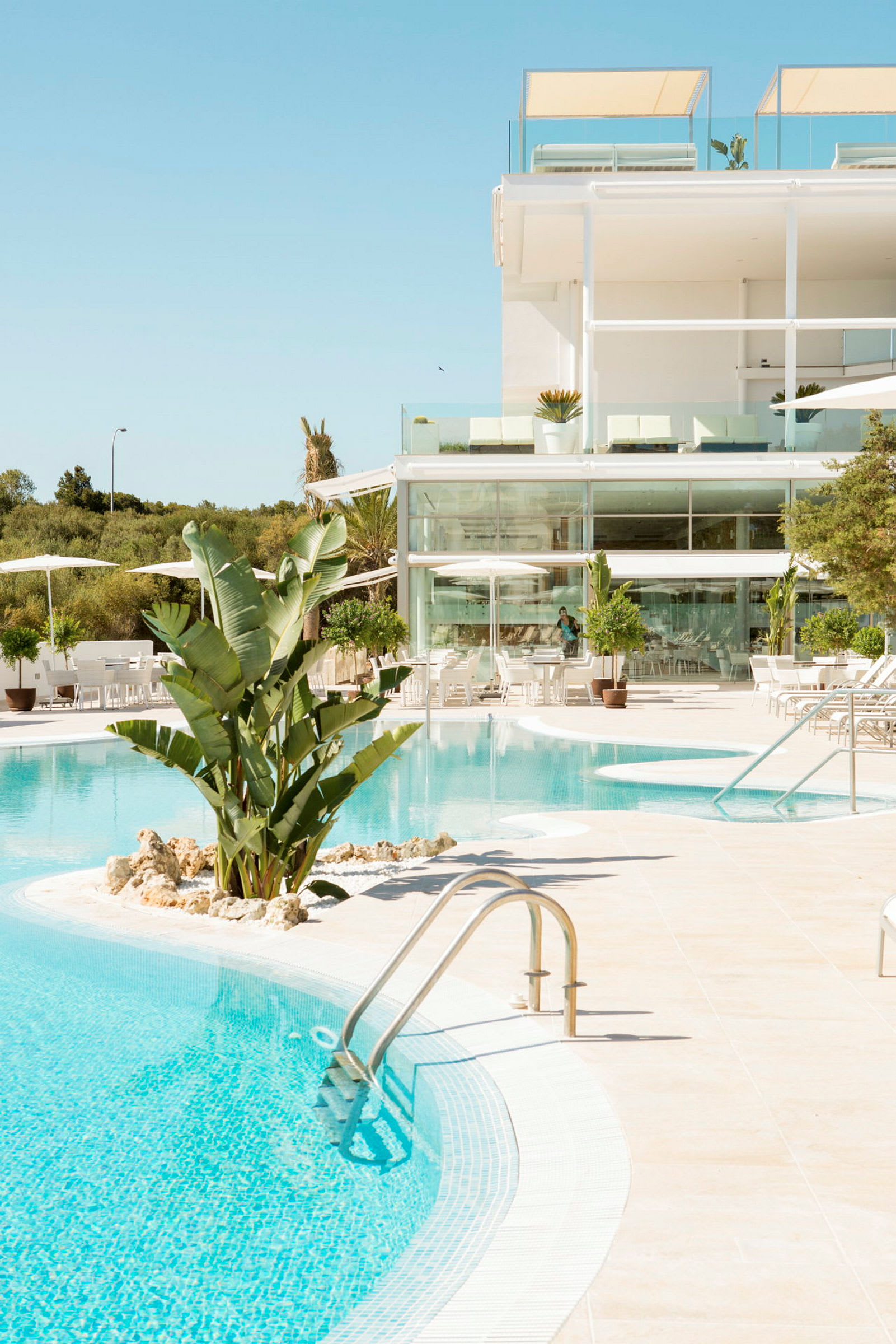 En pool med kristallklart vatten och omgivande solstolar framför en modern byggnad med glasfönster. (AI-genererad text)