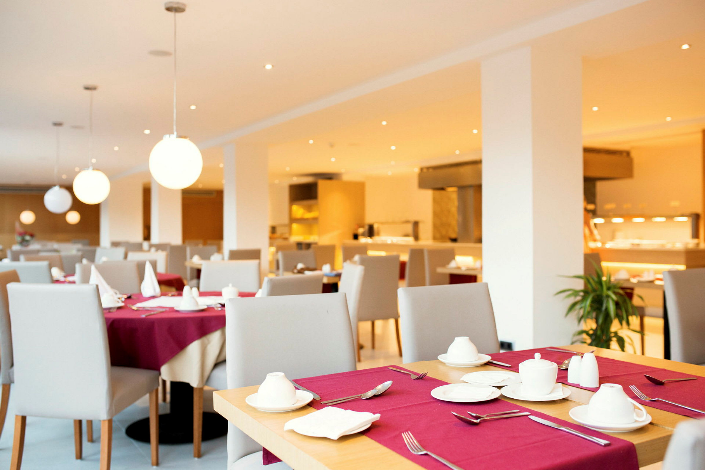 Ett modernt restaurangutrymme med dukade bord och vita lampor som hänger från taket. (AI-genererad text)