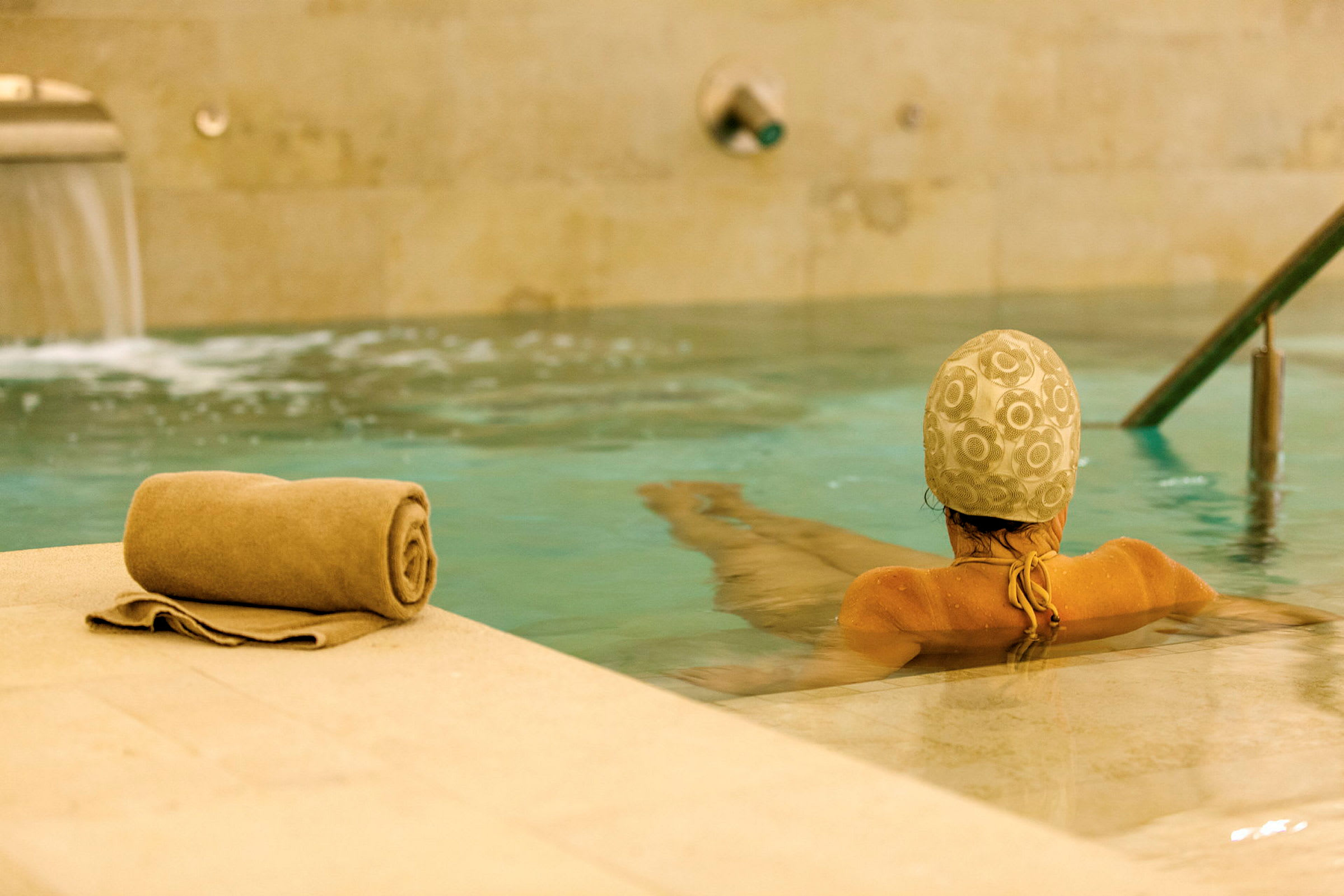 En person med badmössa sitter i en pool, med en hoprullad handduk på kanten. (AI-genererad text)
