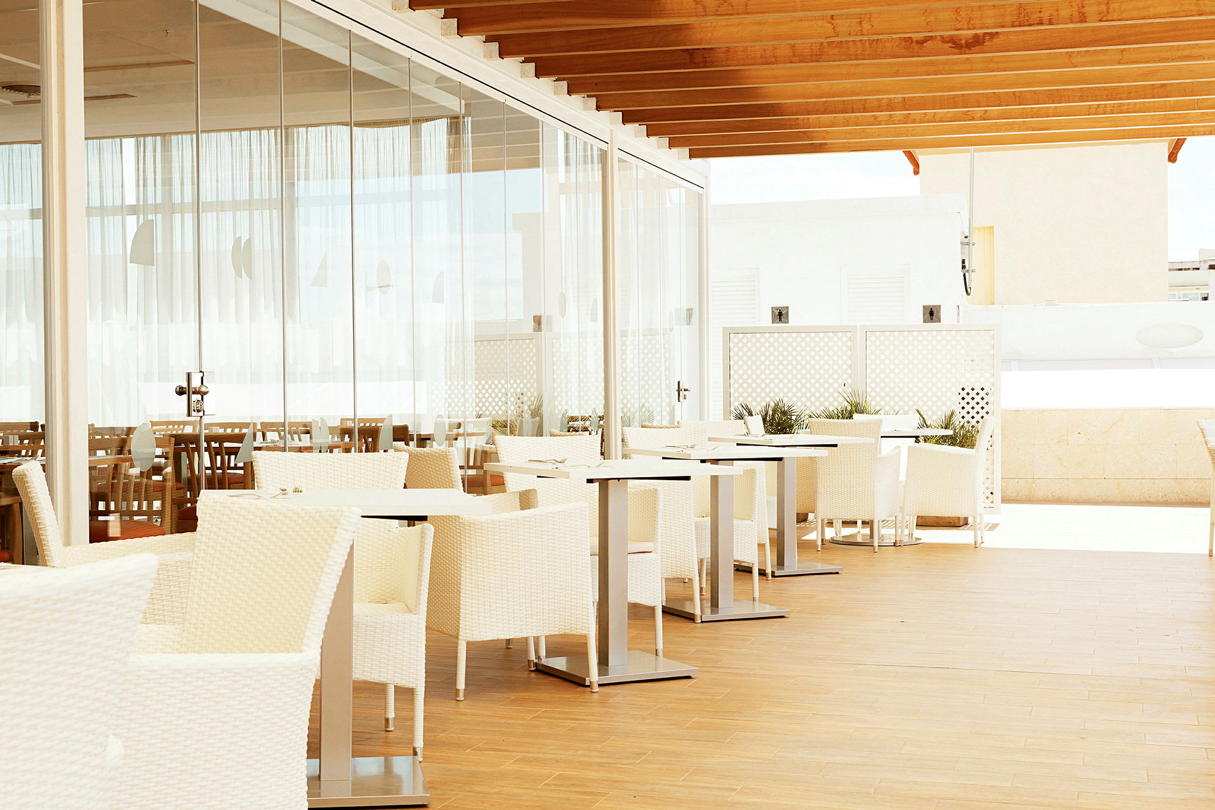 Utomhusrestaurang med vita möbler och glasvägg. (AI-genererad text)