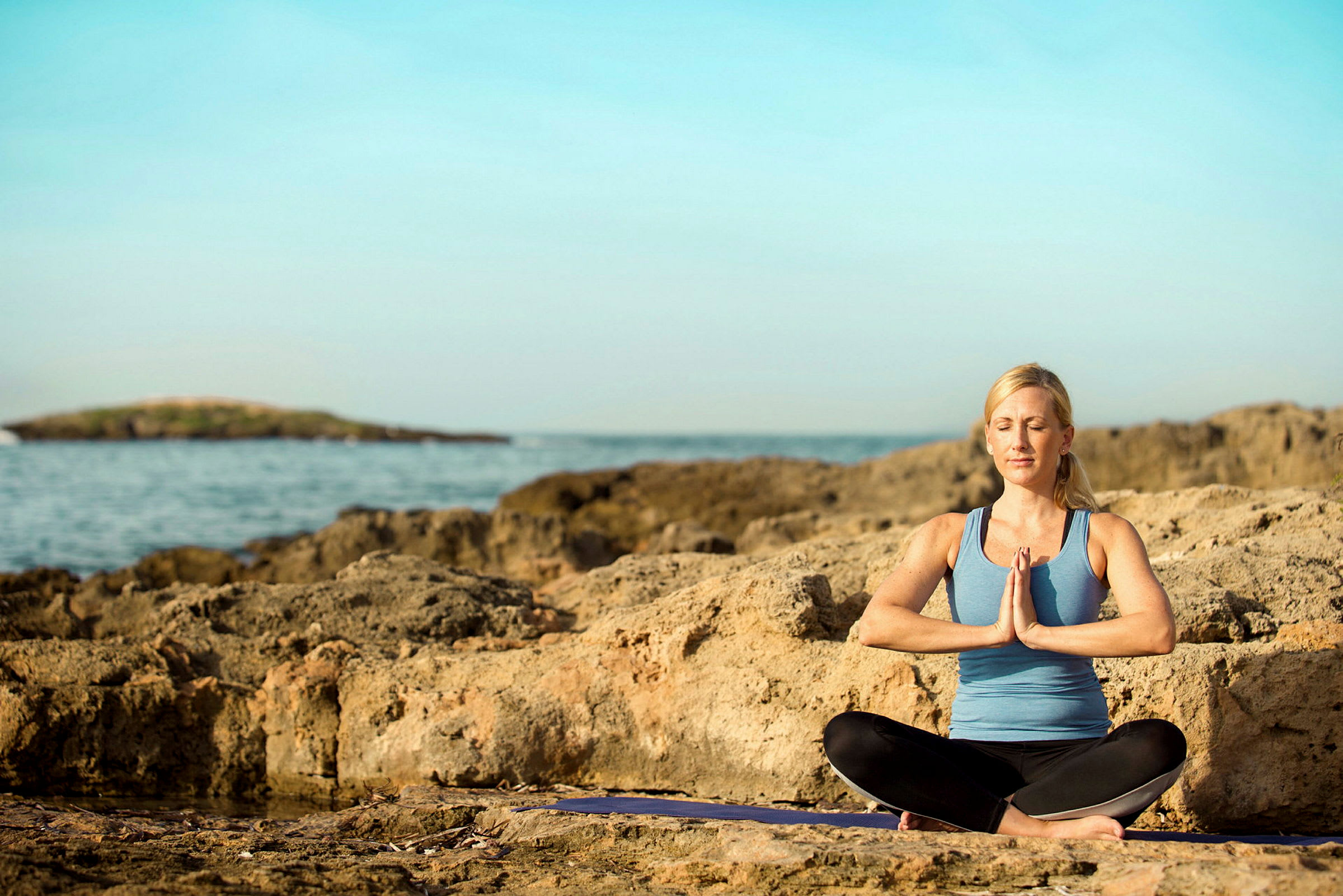 Person i träningskläder sitter i meditationspose på en klippa vid havet. (AI-genererad text)