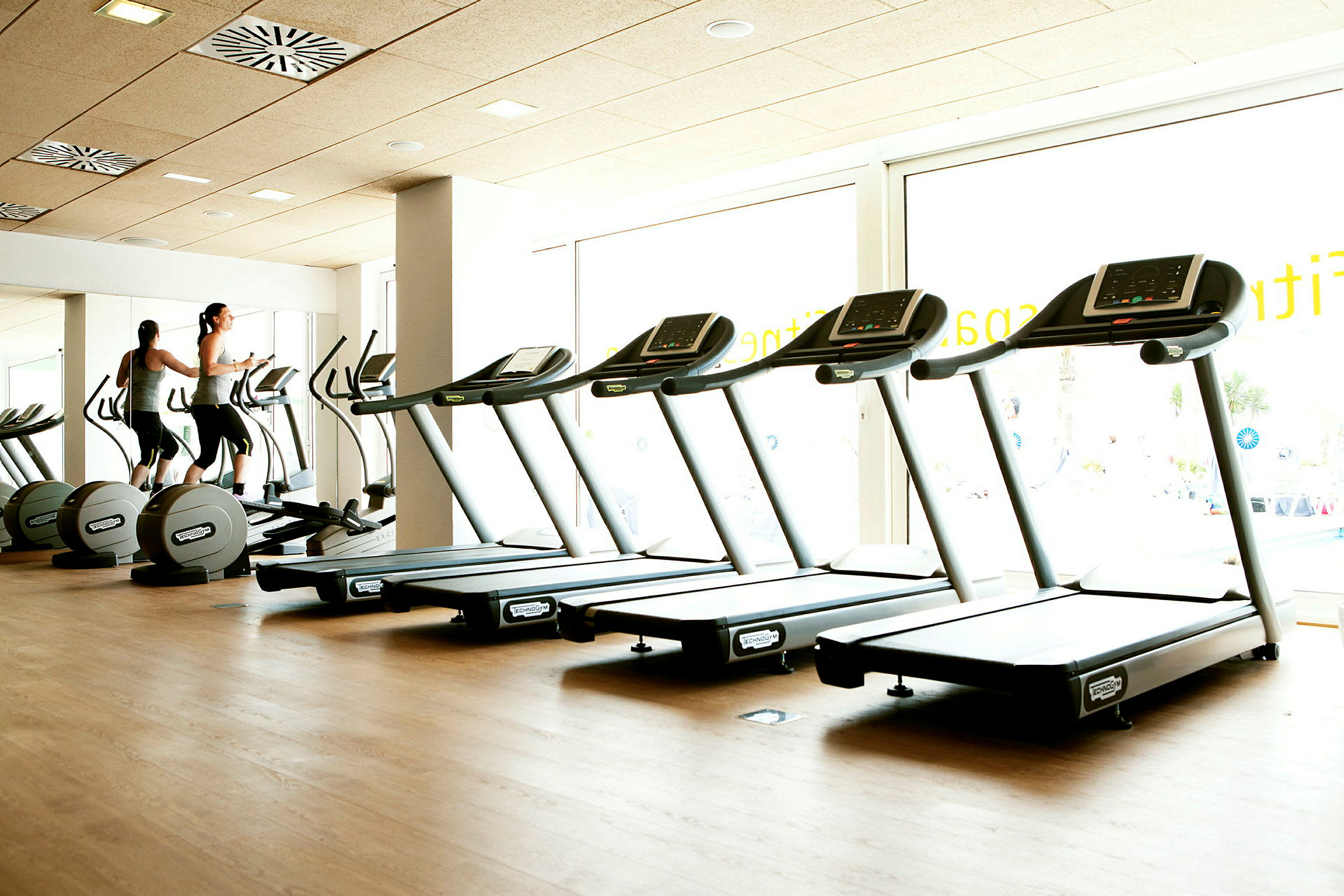Ett gym med löpband och motionscyklar, ljus interiör med stora fönster. (AI-genererad text)