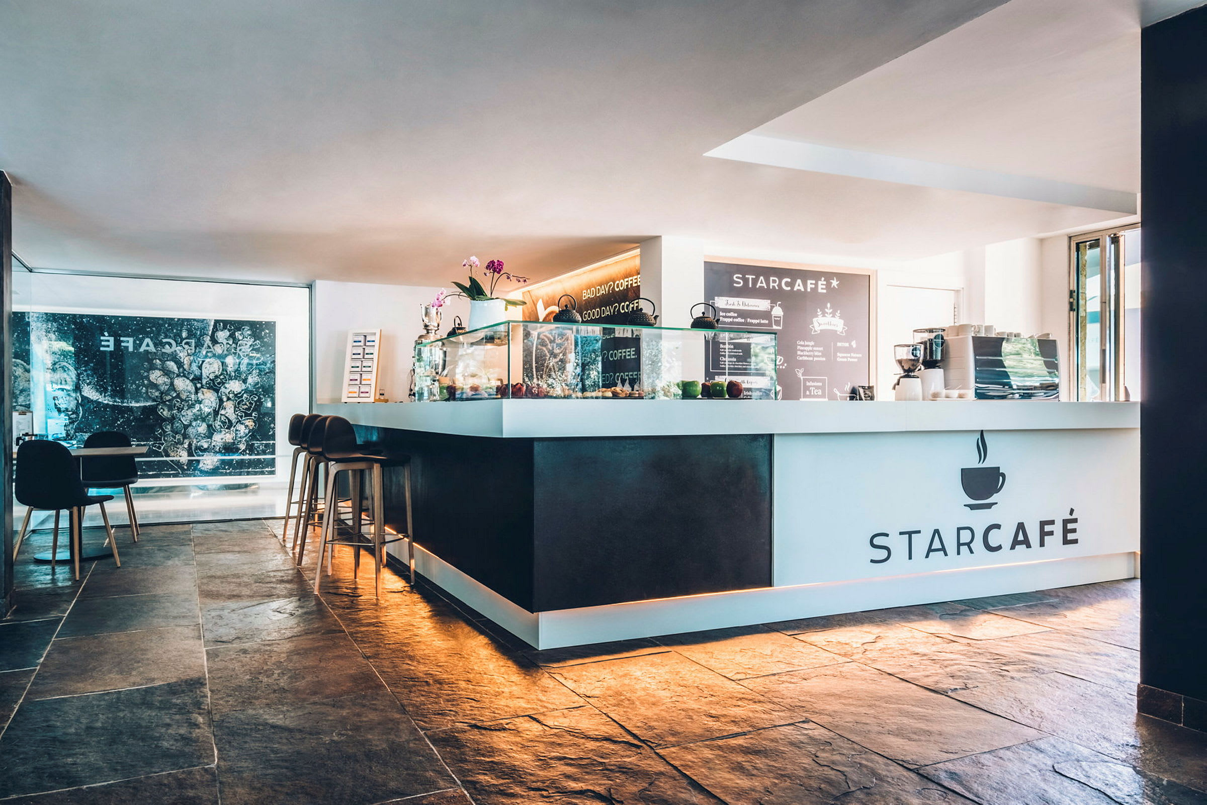 Ett modernt kafé med en vit disk med texten "StarCafé" och en meny på väggen bakom. (AI-genererad text)