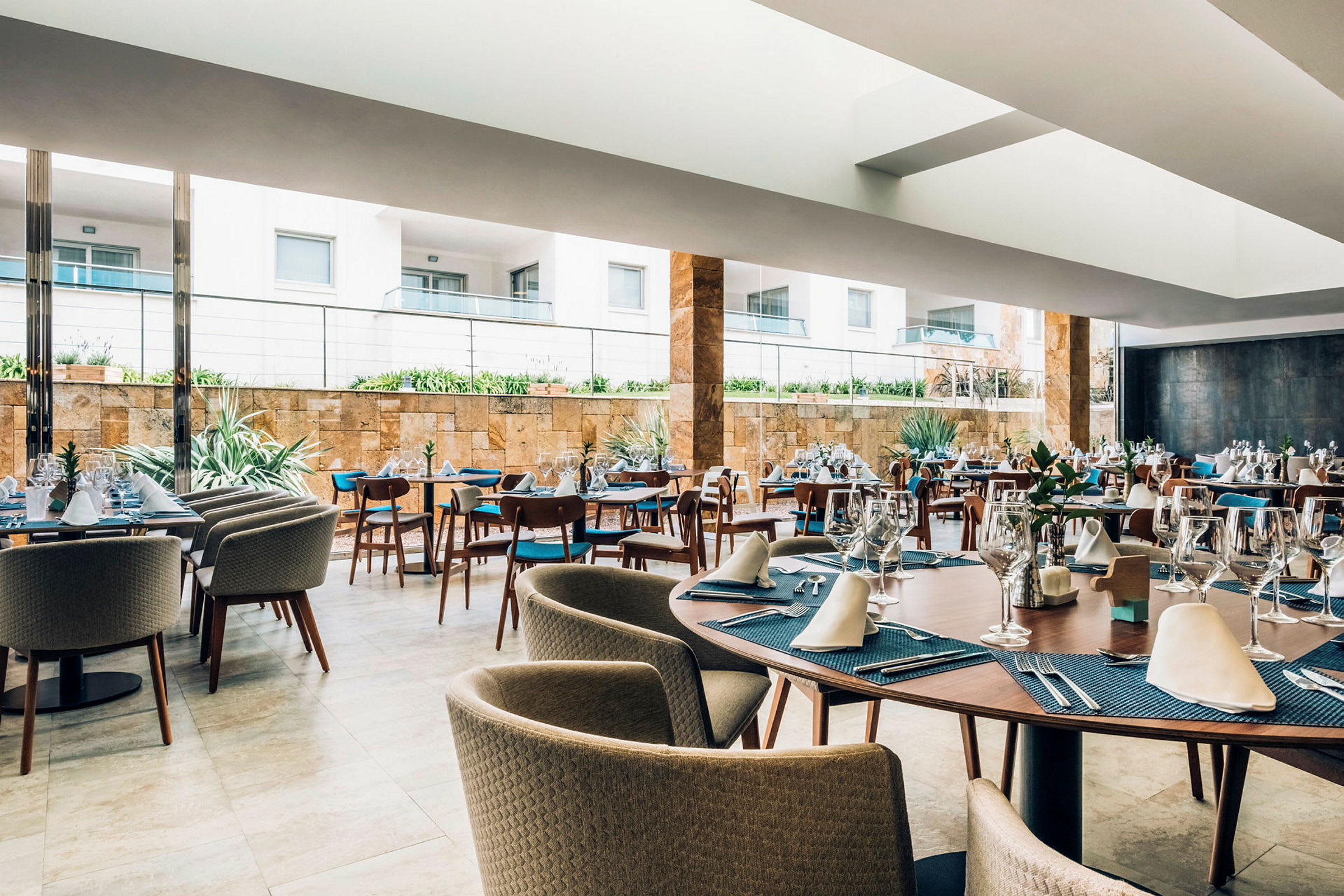 En modern restaurang med uppdukade bord och stolar inomhus, ljusa fönster med utsikt mot en terrass. (AI-genererad text)