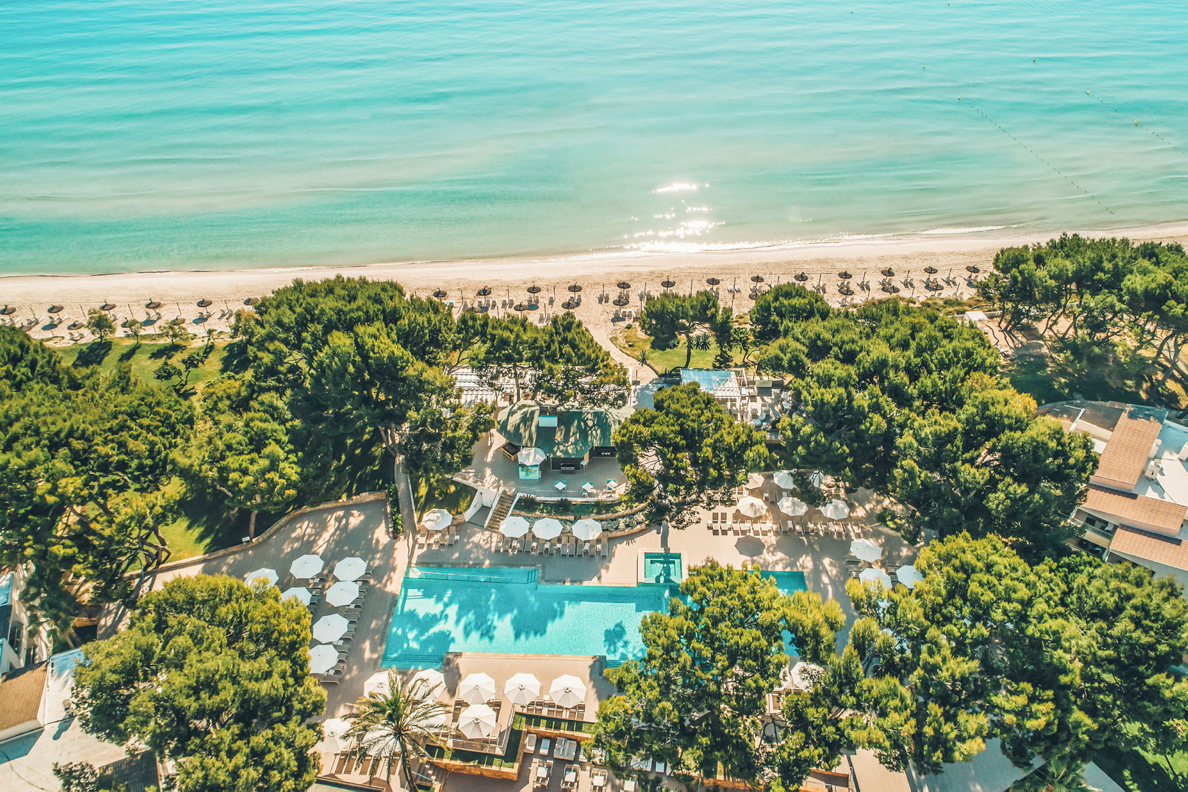 Flygfoto av en strandresort med pool, omgiven av träd och stranden i bakgrunden. (AI-genererad text)