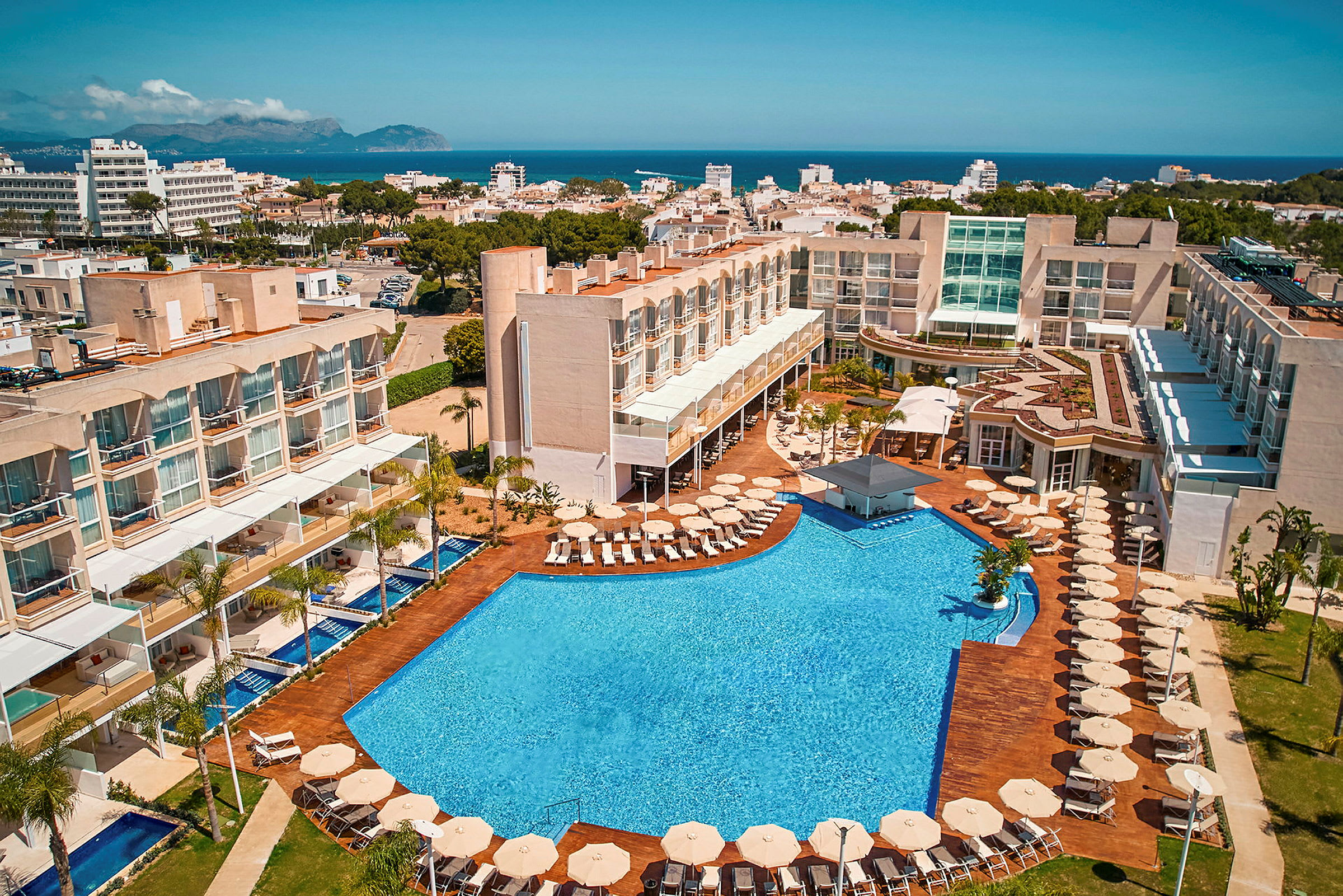Ett hotellkomplex med pool och solstolar, beläget nära en kuststad. (AI-genererad text)