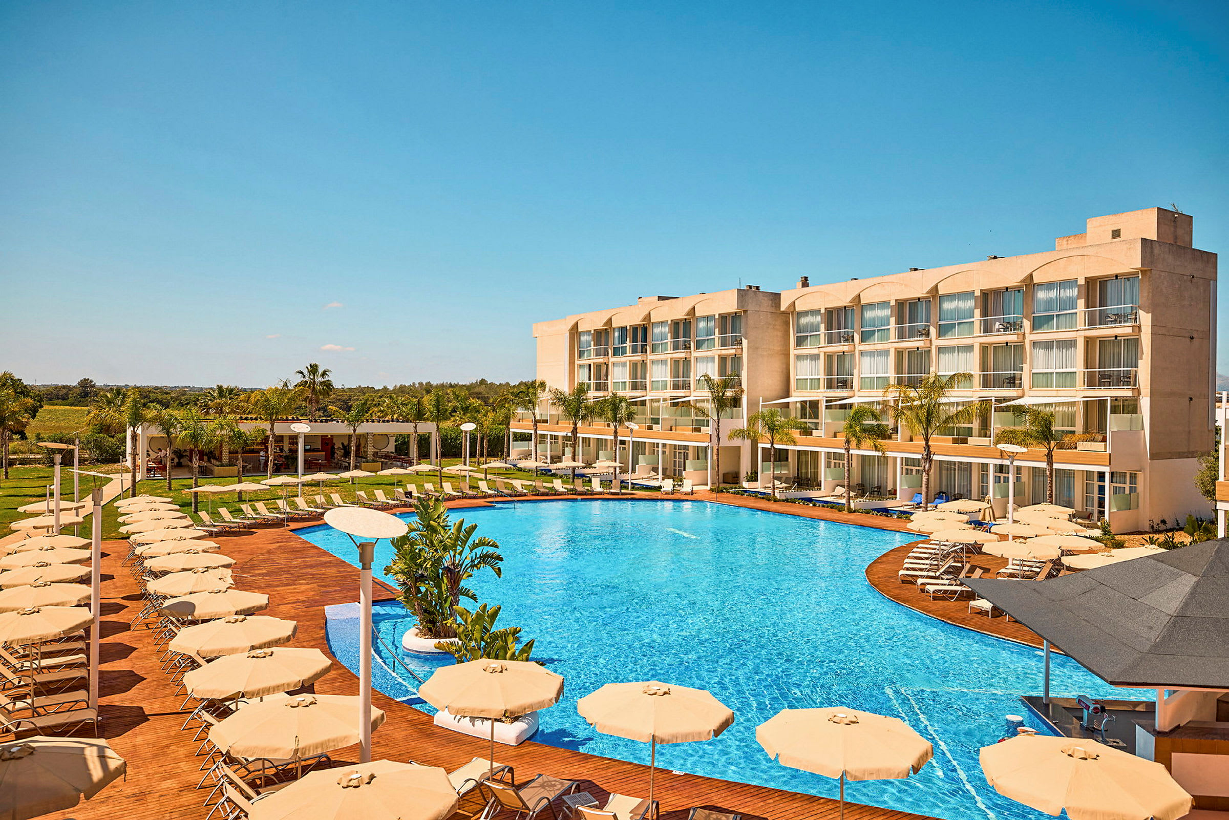 Bild av ett hotell med en stor pool, solstolar och parasoller. (AI-genererad text)