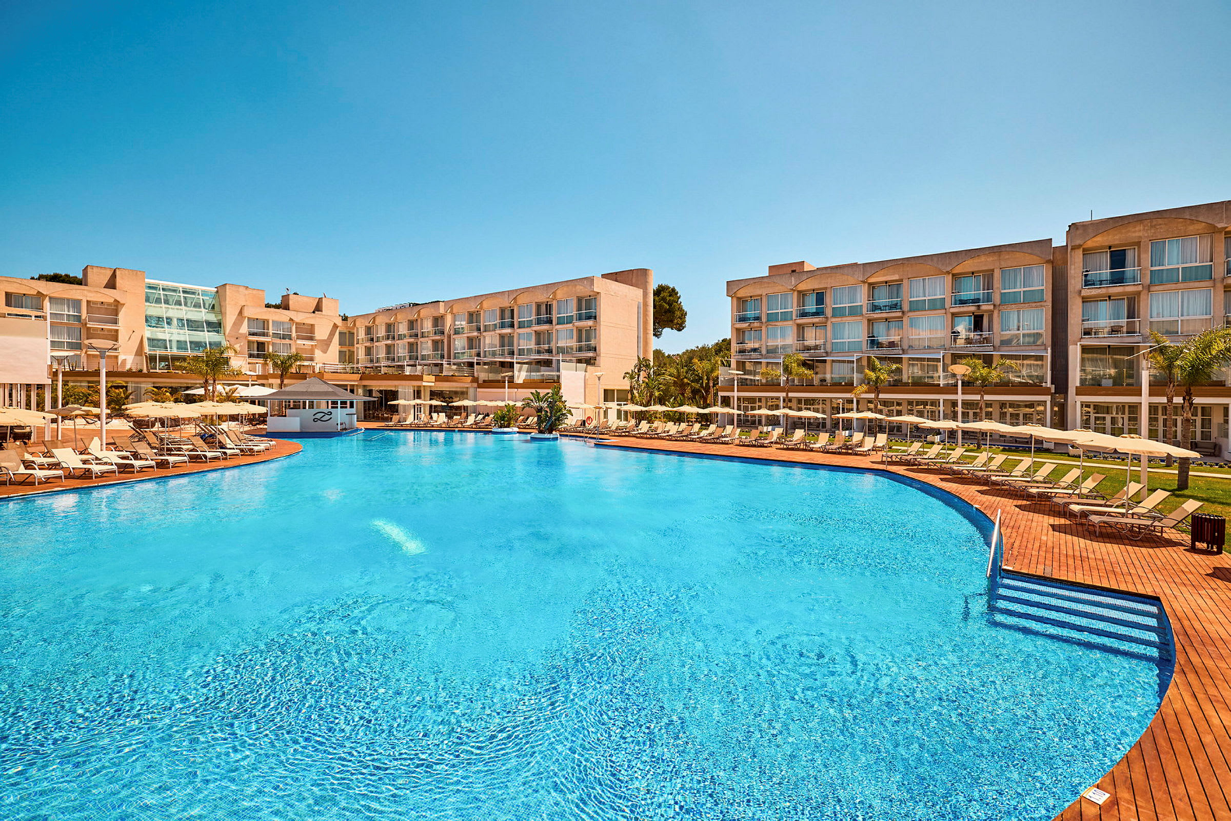 Hotellbyggnader vid en stor pool med solstolar och parasoller. (AI-genererad text)