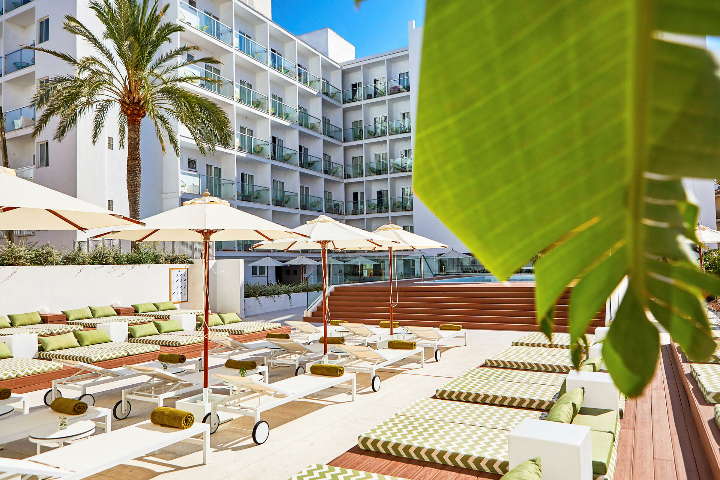 Hotellpoolområde med solstolar, parasoller och ett flervåningshus i bakgrunden. (AI-genererad text)