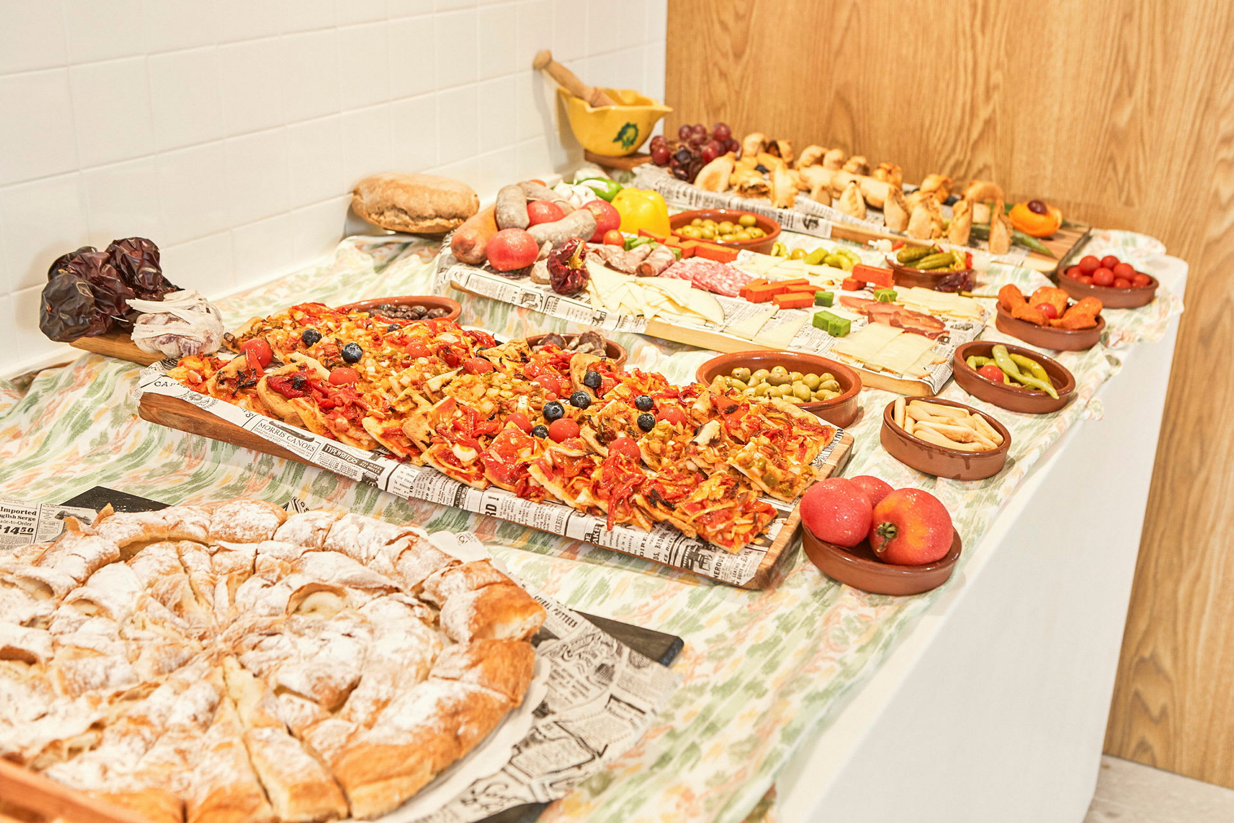Ett bord uppdukat med olika matvaror såsom pizzabitar, bakverk, ost, frukt och grönsaker. (AI-genererad text)
