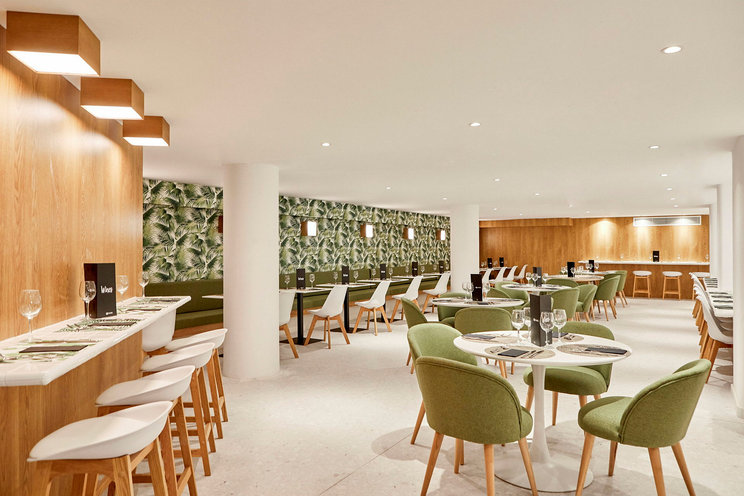 En restauranginteriör med grönmålade stolar och ett tapetserat väggmönster med växtmotiv. (AI-genererad text)