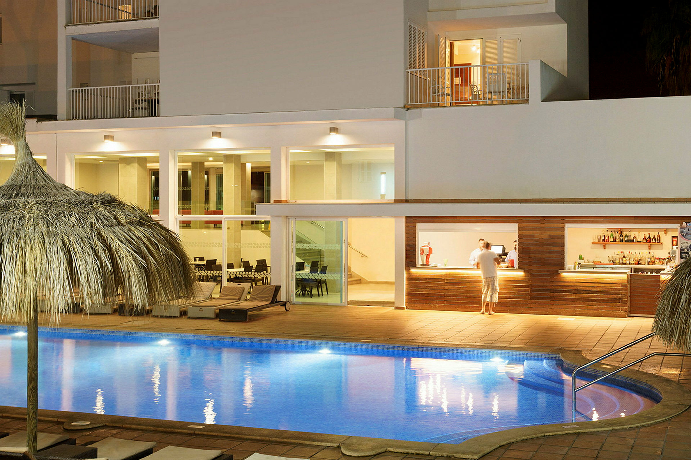Bild på en upplyst hotellpool, solstolar och en bar. (AI-genererad text)