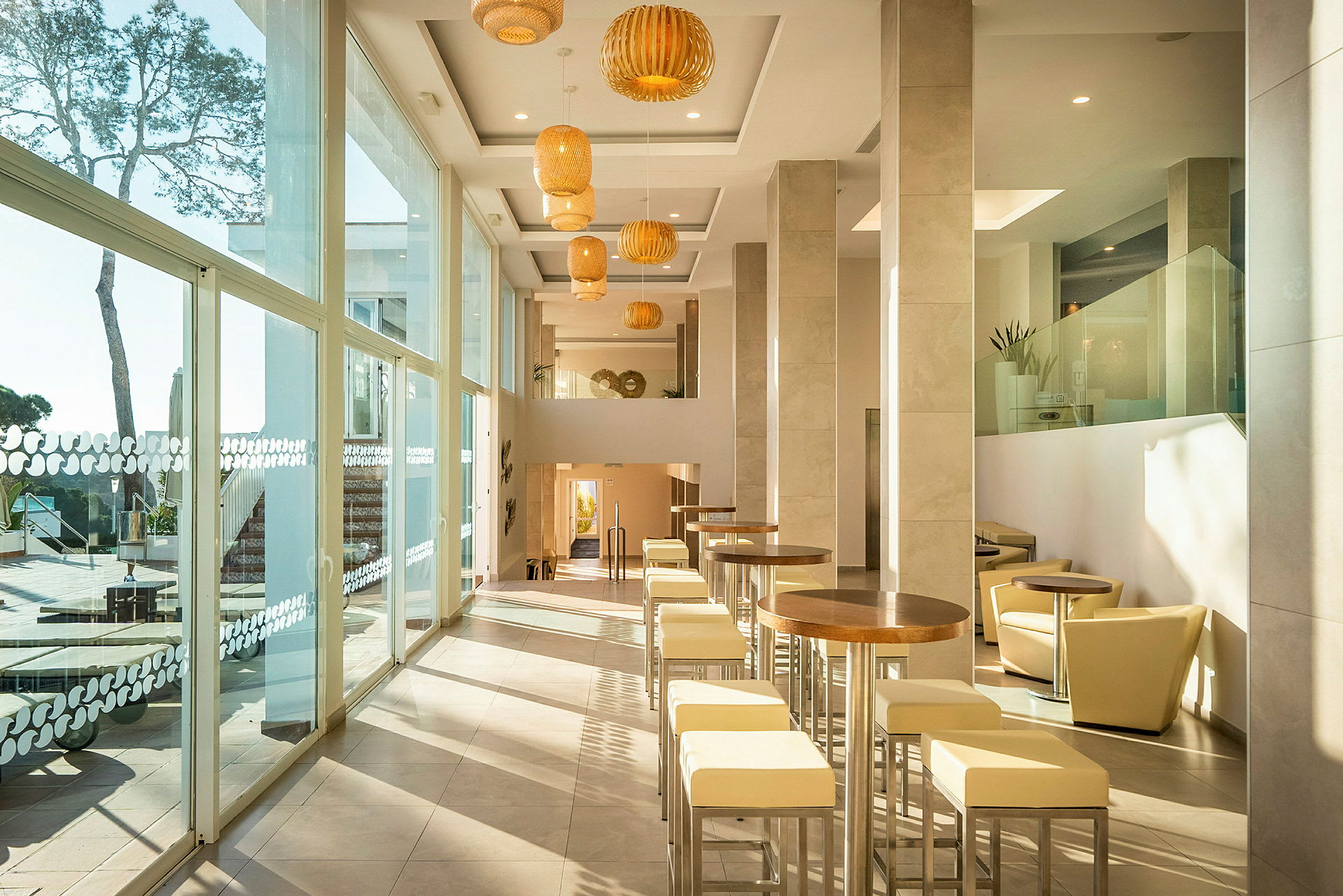 Ljus och modern hotellfoajé med höga fönster, bord och stolar längs ena sidan. (AI-genererad text)