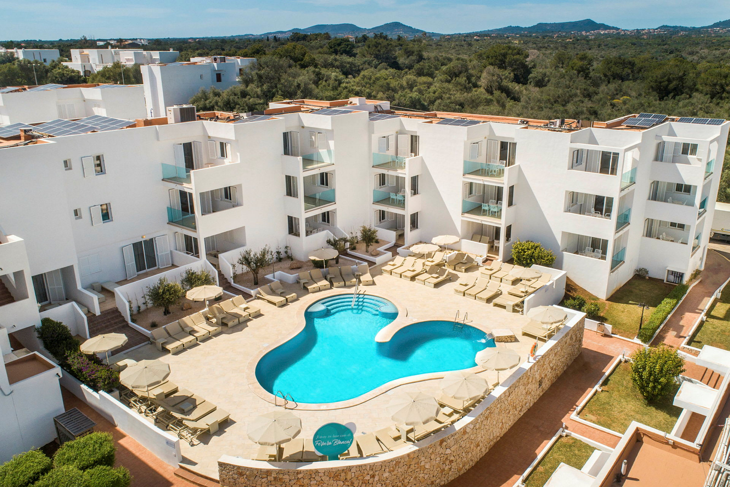 Ett hotellområde med en utomhuspool och solsängar omgivna av vit arkitektur. (AI-genererad text)