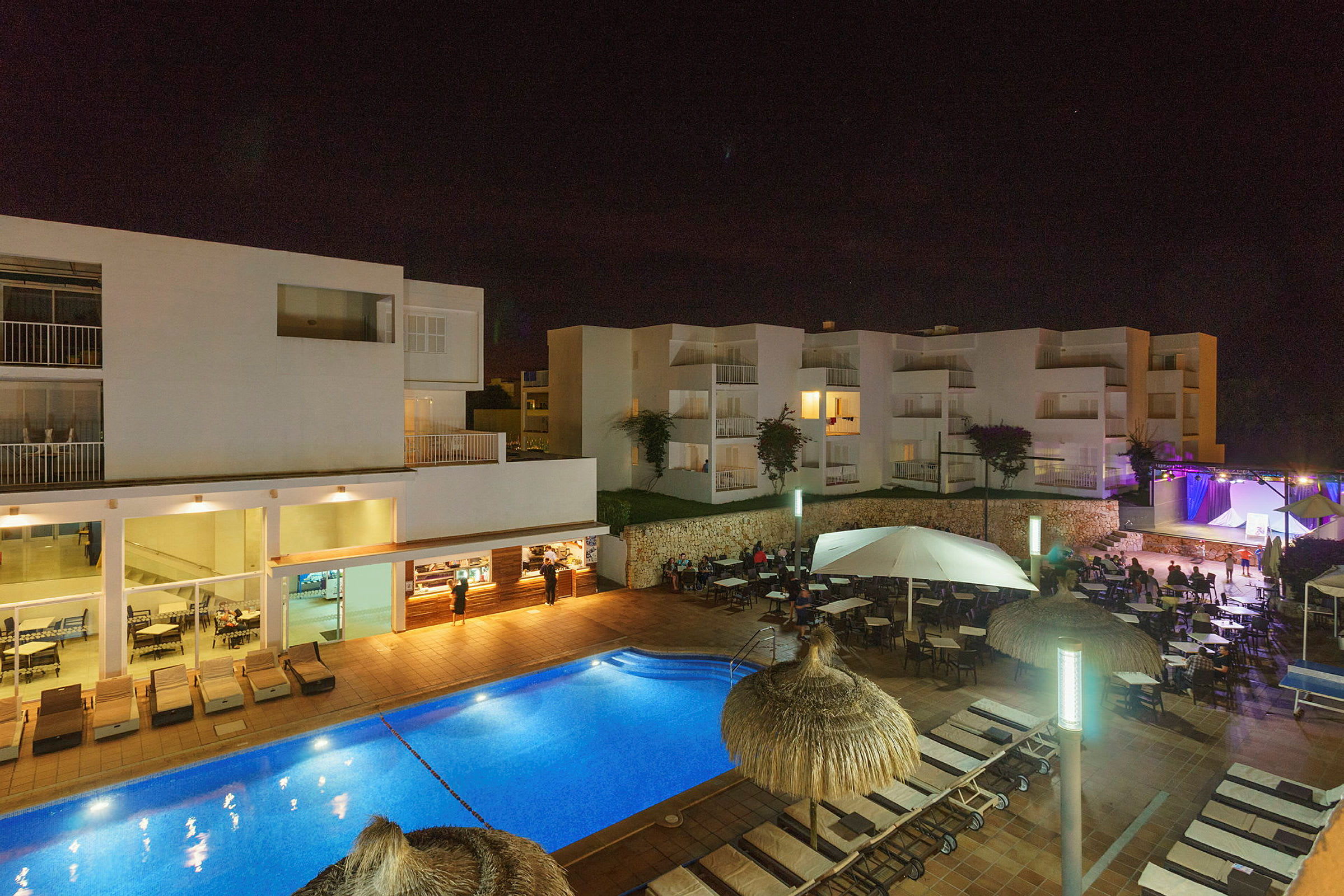 Nattvy av hotellområde med pool, solstolar och byggnader. (AI-genererad text)