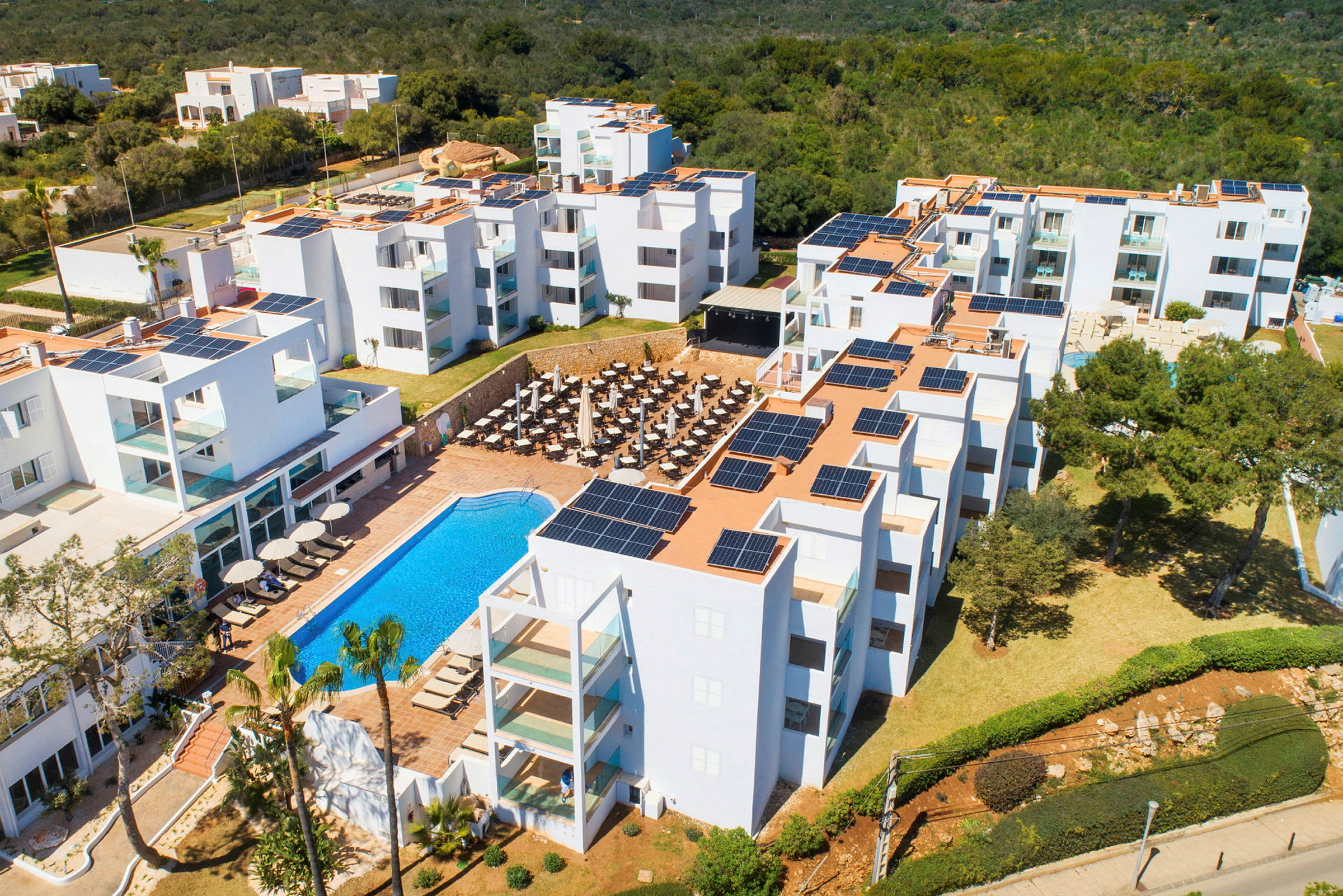 Ett hotell med vita byggnader, en pool och solarpaneler på taken. (AI-genererad text)
