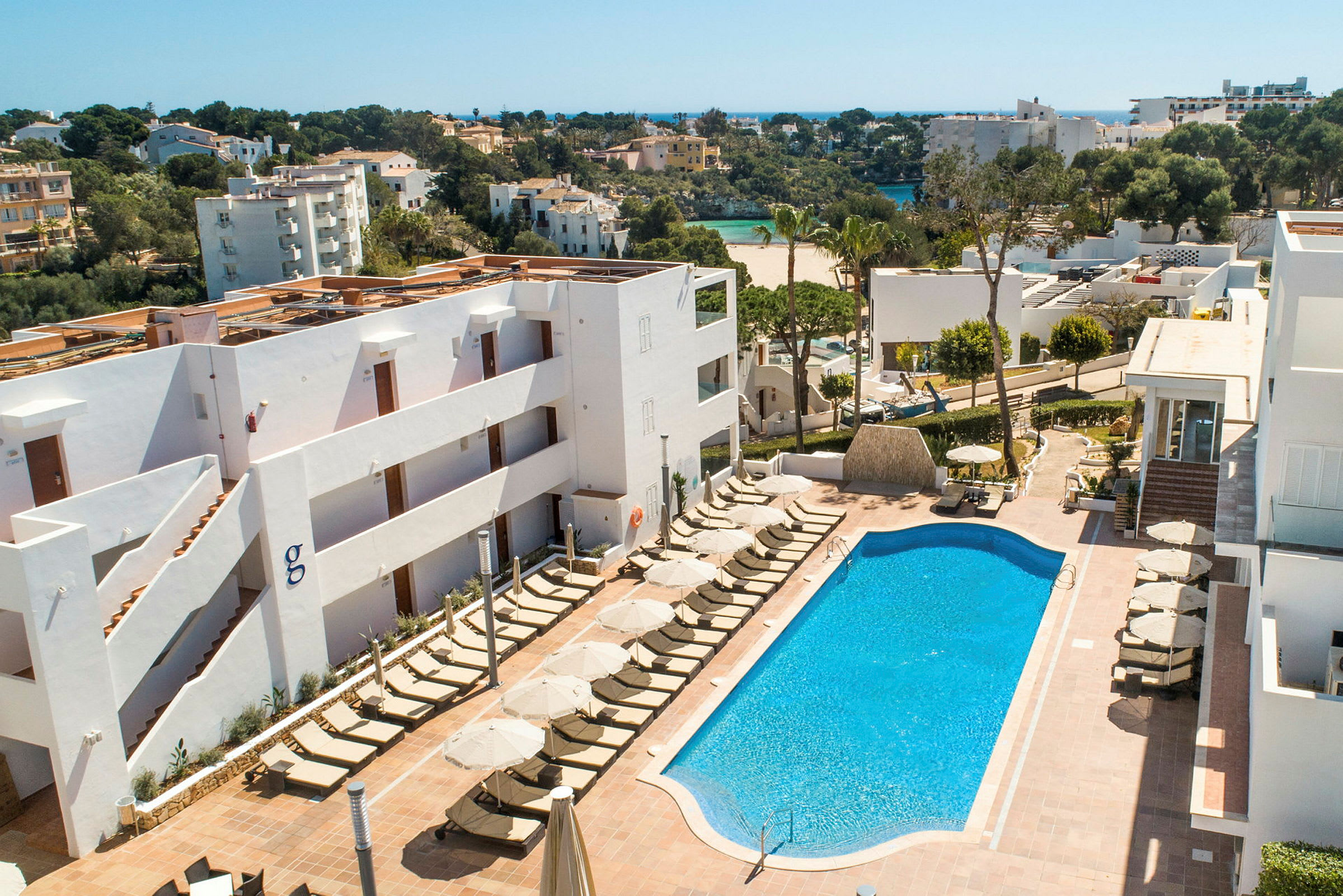 Bild av ett hotellområde med en pool och solstolar. I bakgrunden syns grönområden och byggnader. (AI-genererad text)