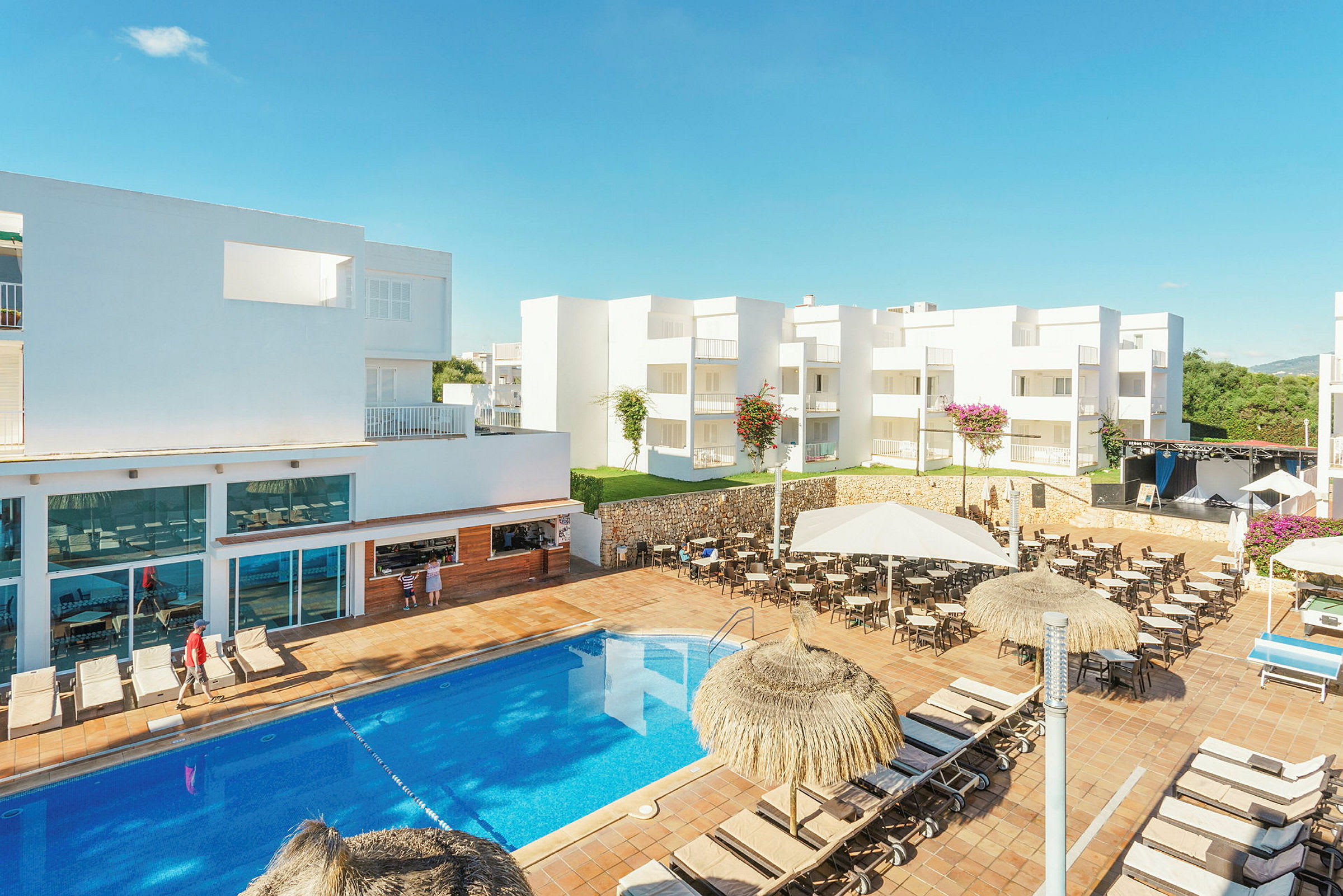 Bild av ett hotellområde med vitmålade byggnader, pool och solstolar. (AI-genererad text)