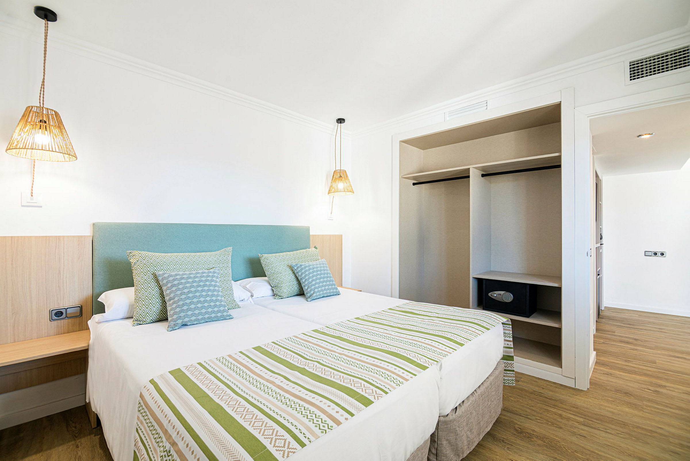 Ett hotellrum med en dubbelsäng, sänglampor och en öppen garderob. (AI-genererad text)
