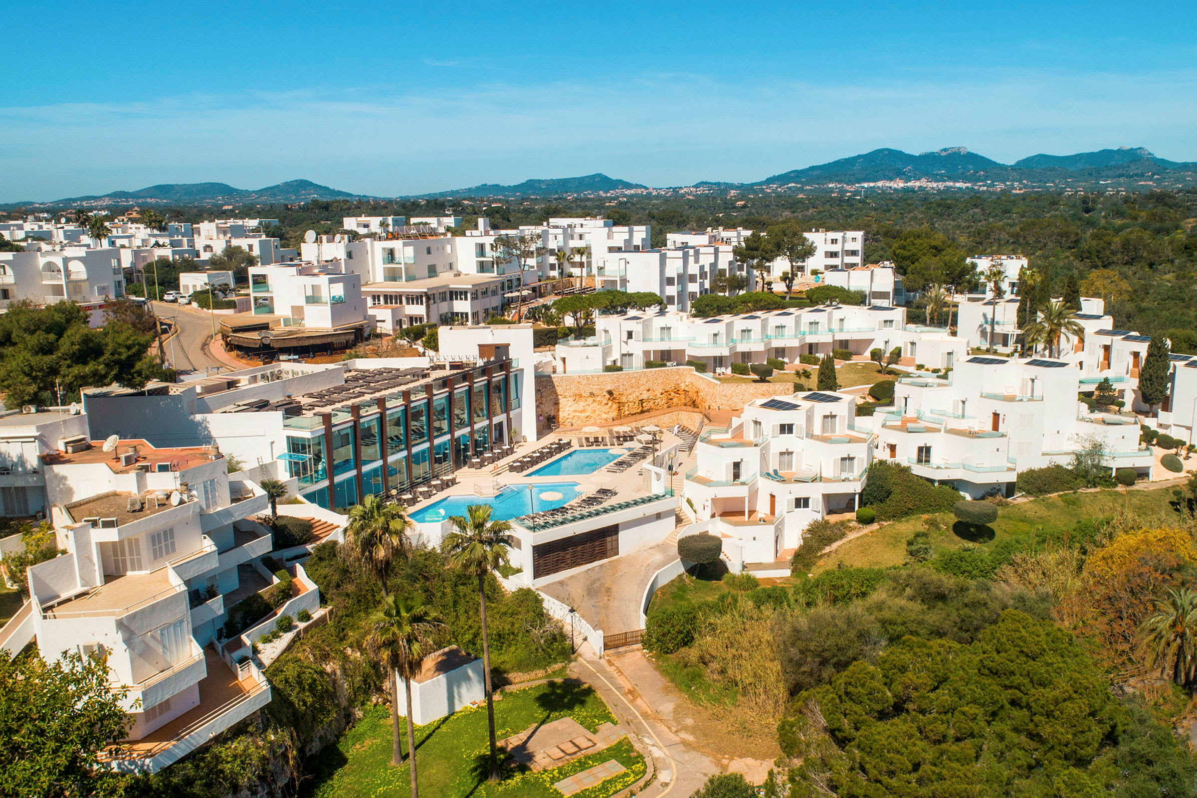 Hotellkomplex med vita byggnader, pool och grönska i förgrunden. (AI-genererad text)