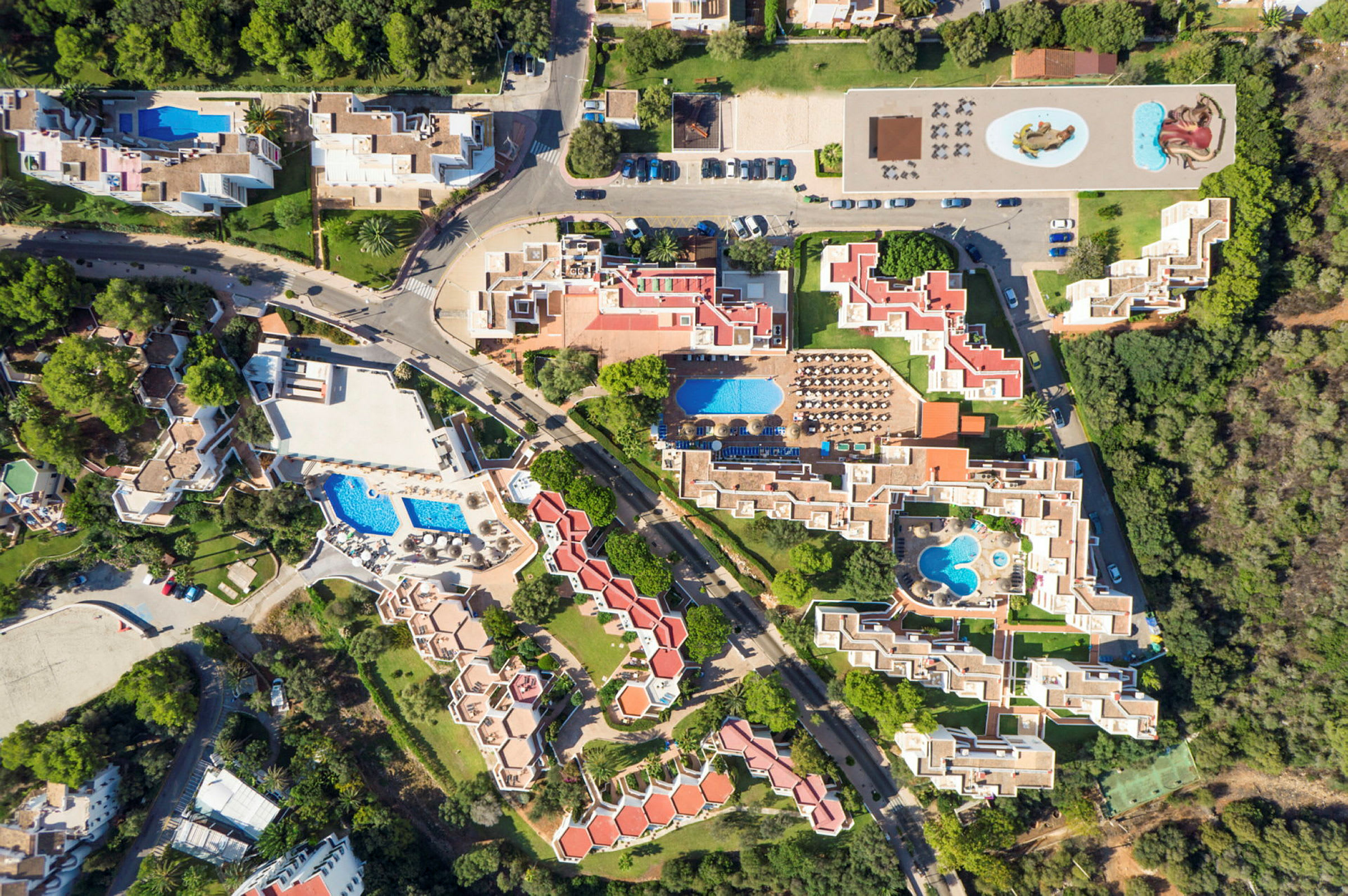 Flygfoto över ett hotellkomplex med flera pooler, byggnader och gröna områden. (AI-genererad text)