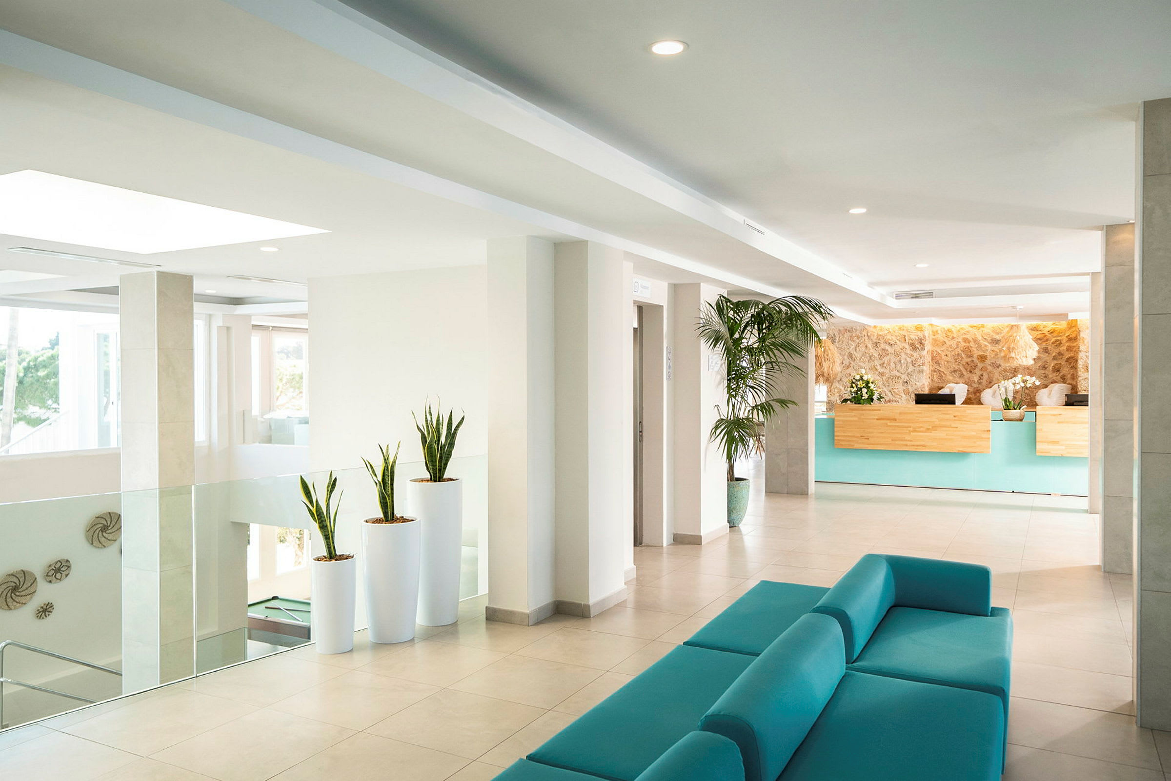 Hotelllobby med turkos soffgrupp, reception och dekorativa växter. (AI-genererad text)