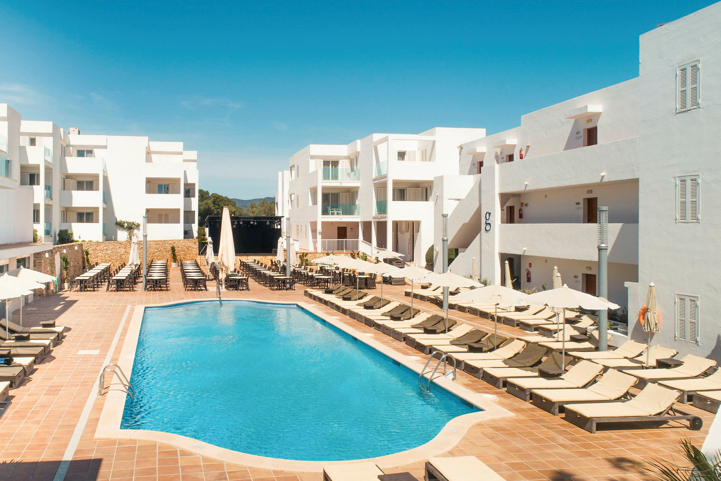 Vit hotellbyggnad med utomhuspool och solstolar. (AI-genererad text)