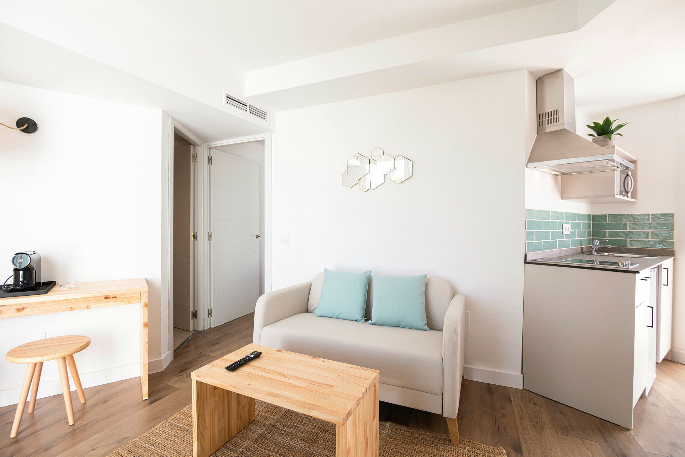 Modernt inrett vardagsrum med beige soffa, träbord, och en liten köksdel med gröna kakelplattor. (AI-genererad text)