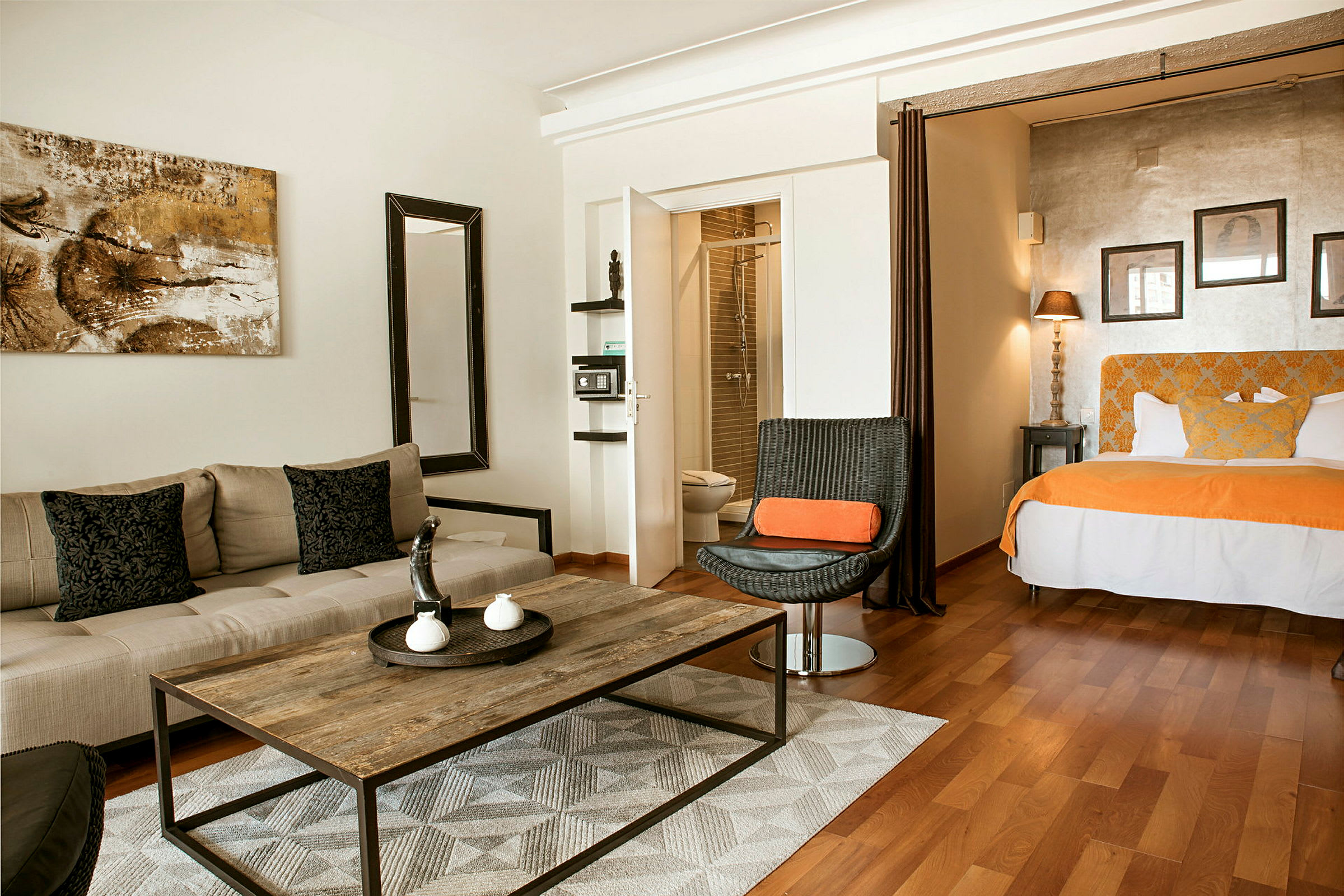 Ett hotellrum med sittmöbler, ett bord, och en säng med orange detaljer. (AI-genererad text)
